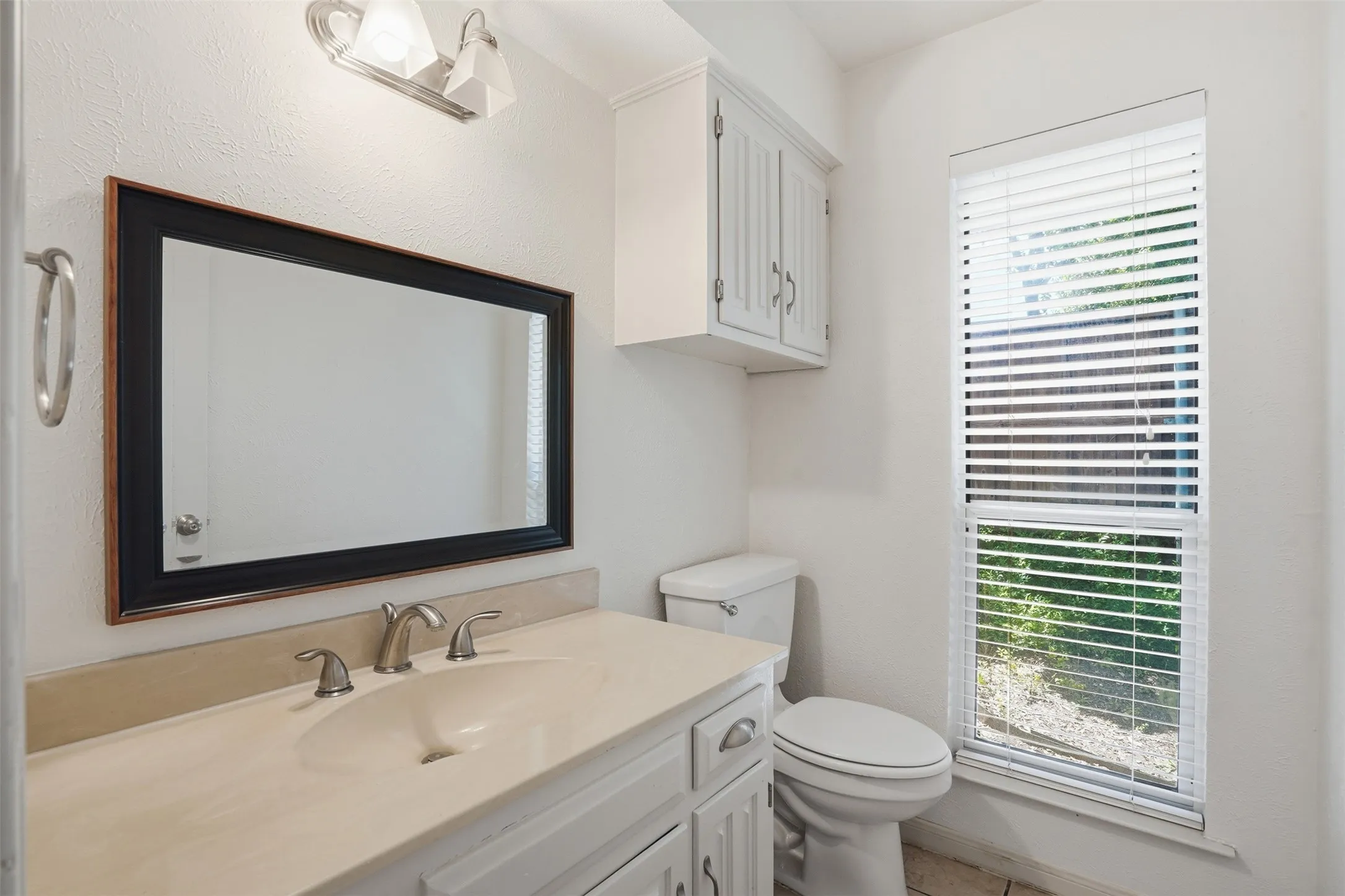 Bathroom featuring a single vanity with an integrated sink, framed mirror, and chrome fixtures