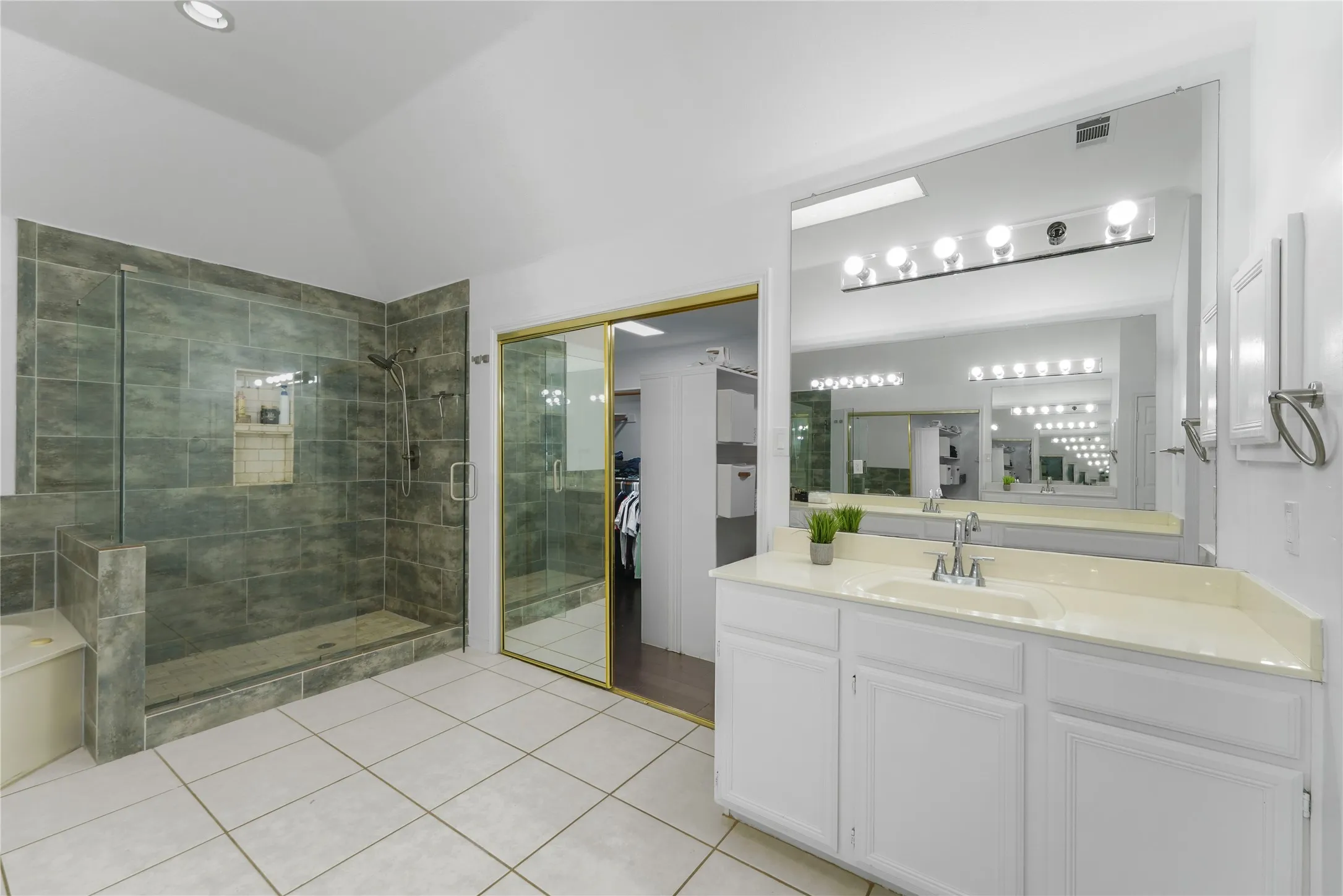 Spacious bathroom featuring a large walk-in shower with stone-look tile, glass enclosure, and built-in bench