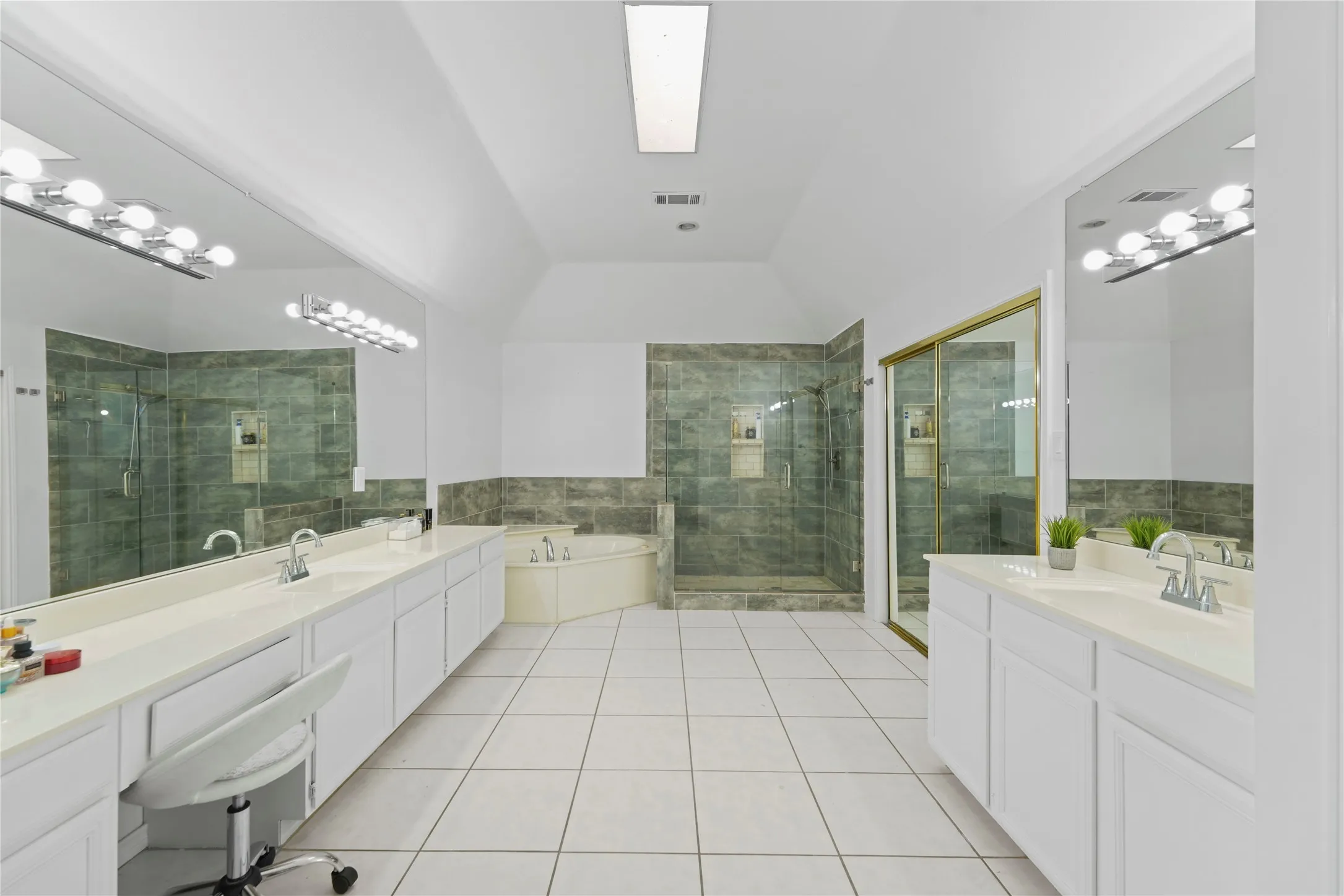 Spacious bathroom featuring dual vanities with white cabinetry and countertops, a built-in corner soaking tub, and a separate tiled shower with a glass enclosure