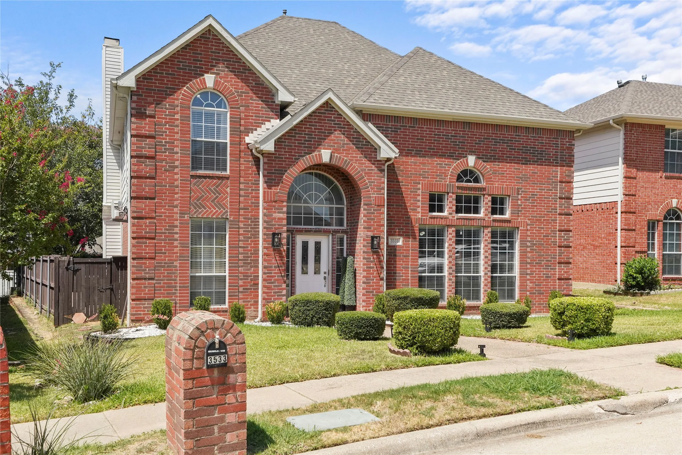 Brick facade residence featuring arched entry, multiple arched windows, mature landscaping, a two-story design, and an attached chimney