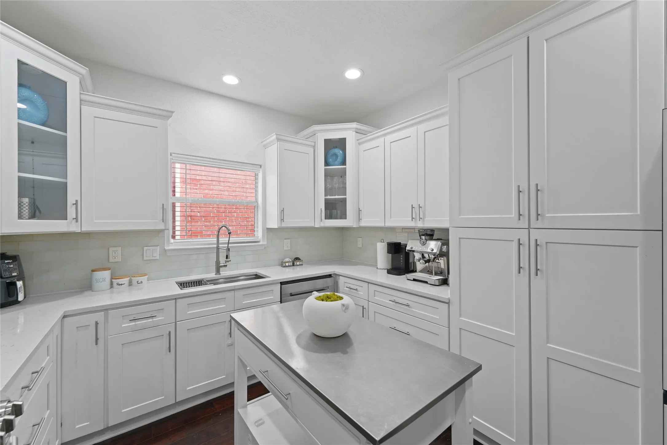 Modern kitchen featuring white shaker-style cabinetry, a central island with a solid surface countertop, recessed lighting, and stainless steel hardware