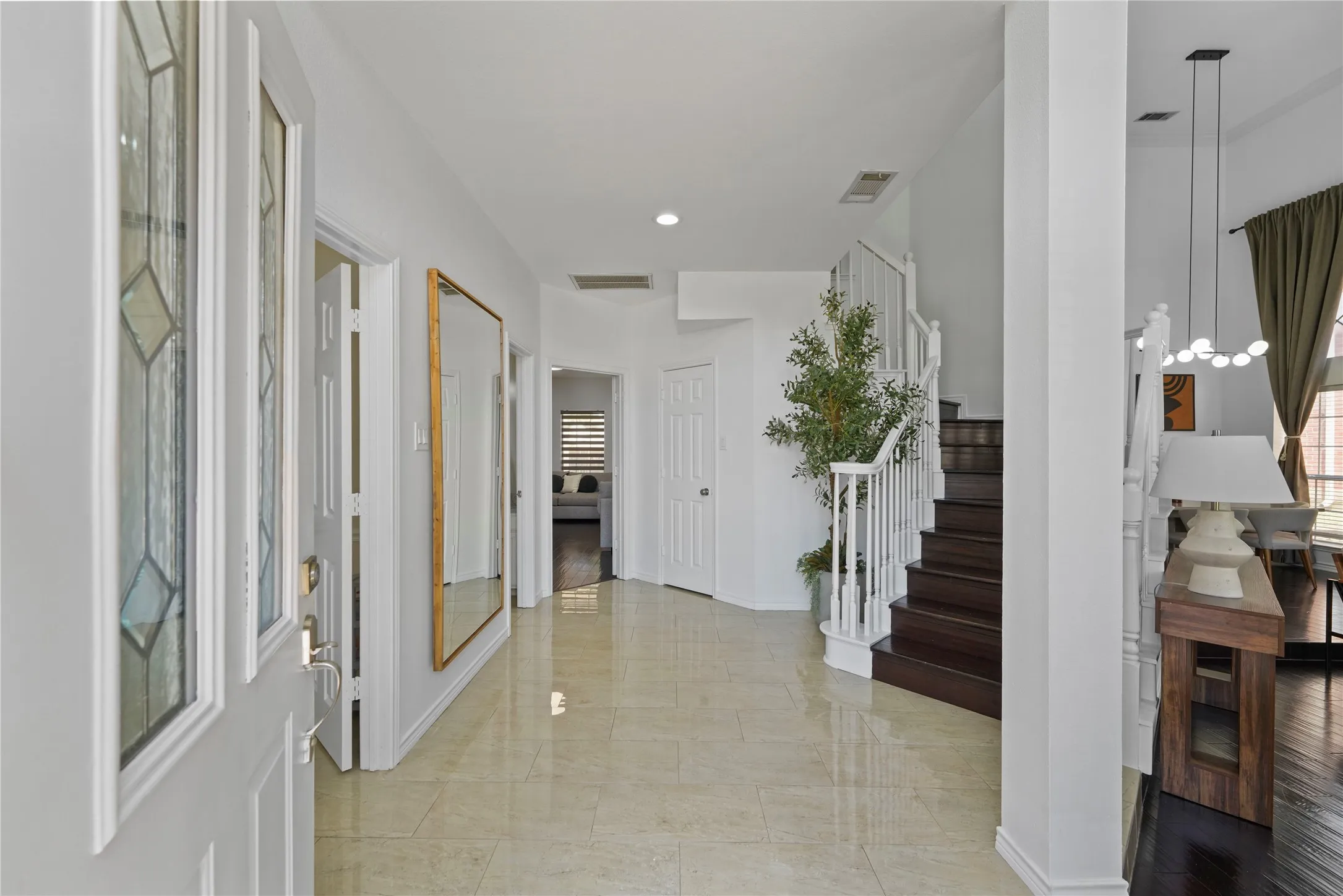 Inviting entryway featuring polished tile flooring, a dark wood-finish staircase with white balusters, and a decorative stained-glass sidelight