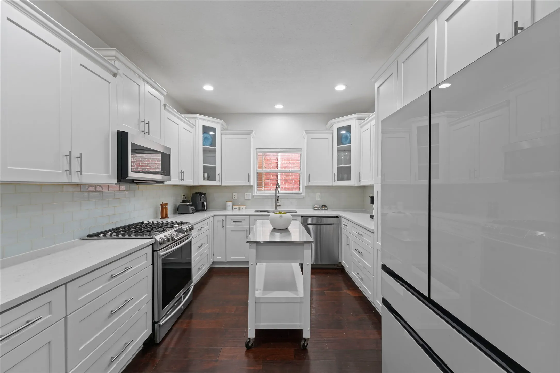 Kitchen featuring white shaker cabinetry with brushed nickel hardware, light-toned countertops, a subway tile backsplash, and wood-finish flooring
