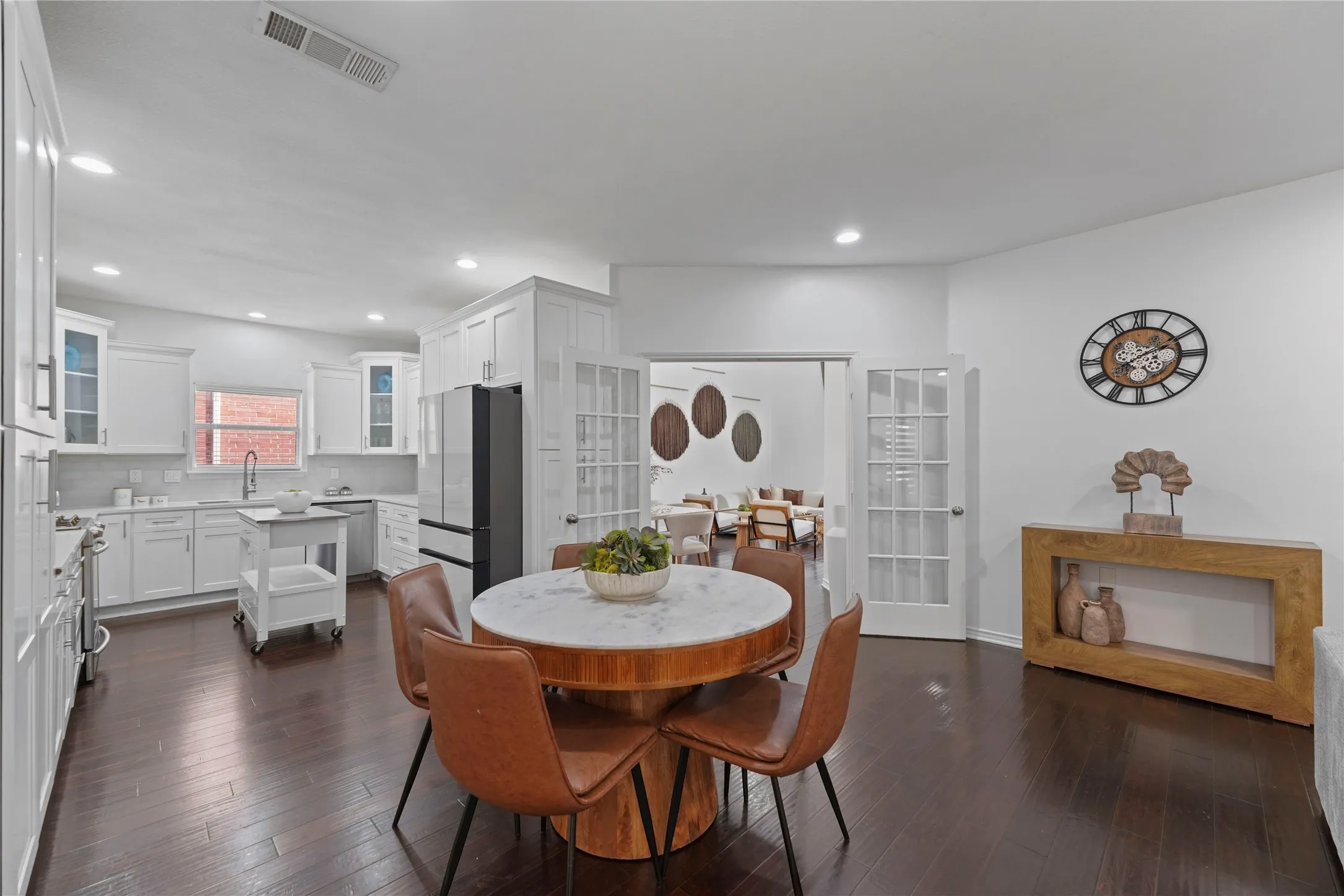 Open-concept kitchen and dining area featuring dark wood-finish flooring, white cabinetry, and a subway tile backsplash