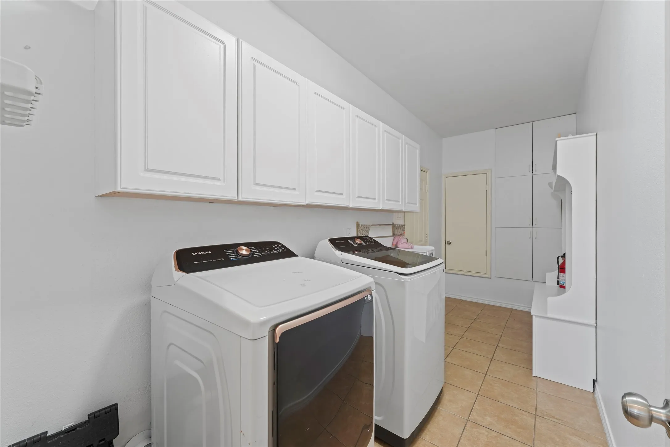 Laundry area featuring abundant white cabinetry, light-toned tile flooring, and a built-in storage bench