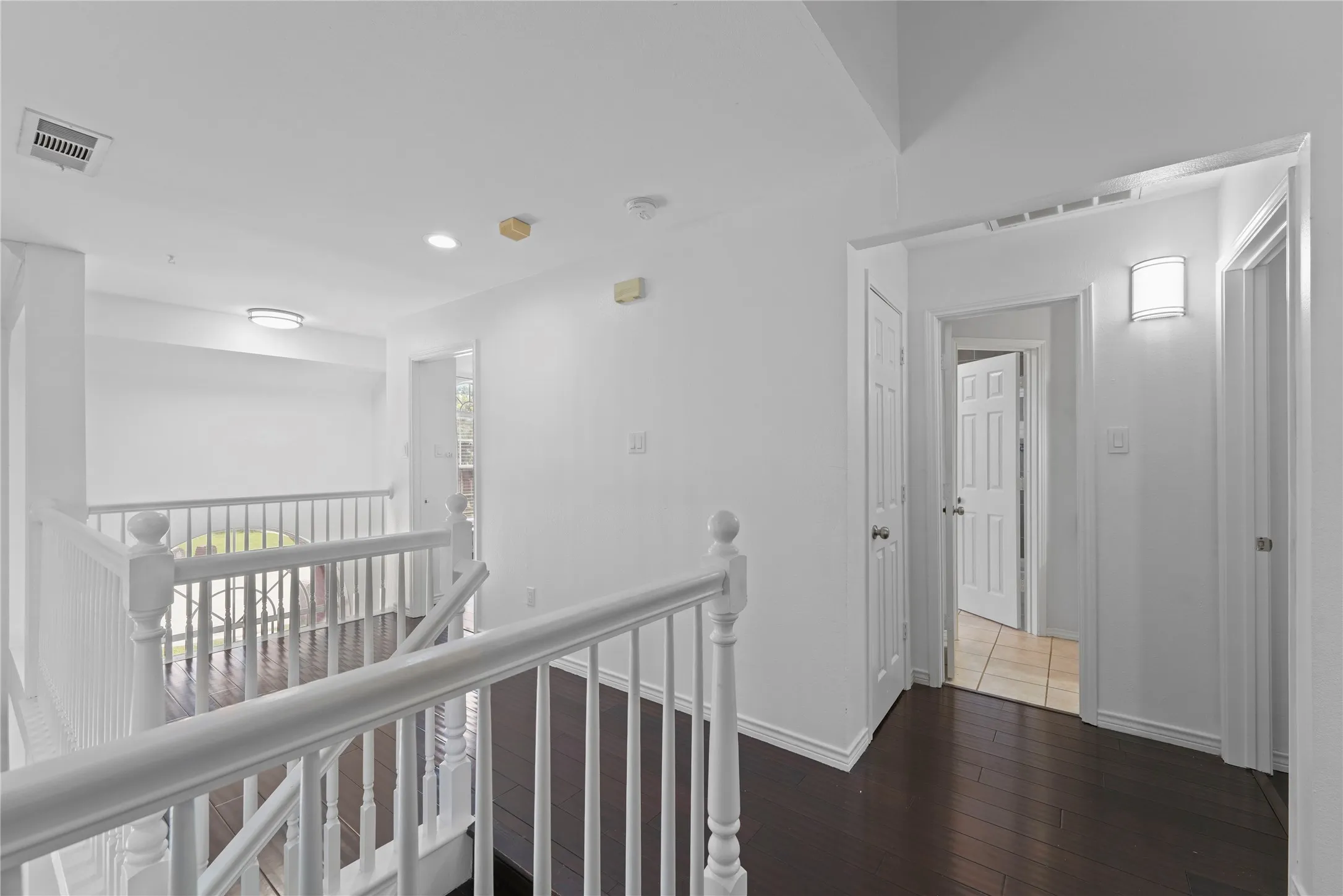 Upper-level corridor featuring dark wood-finish flooring, white walls, and a white baluster railing system