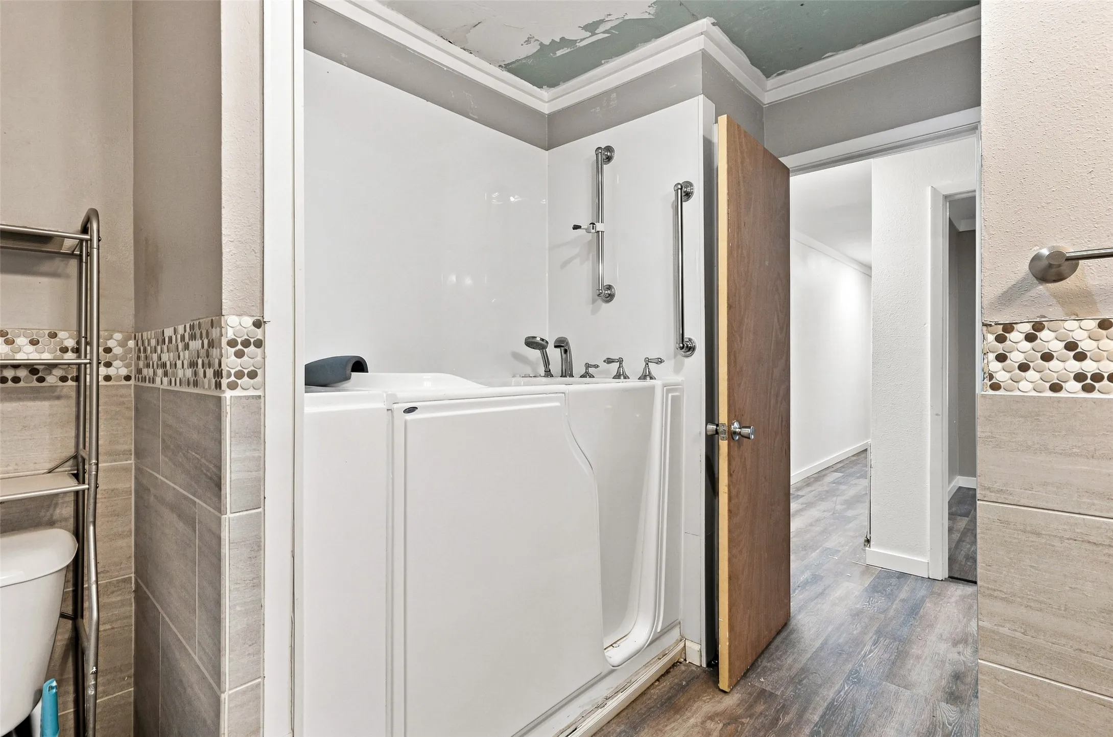 Walk-in tub with grab bars, wood-finish flooring, and wall-mounted towel bar