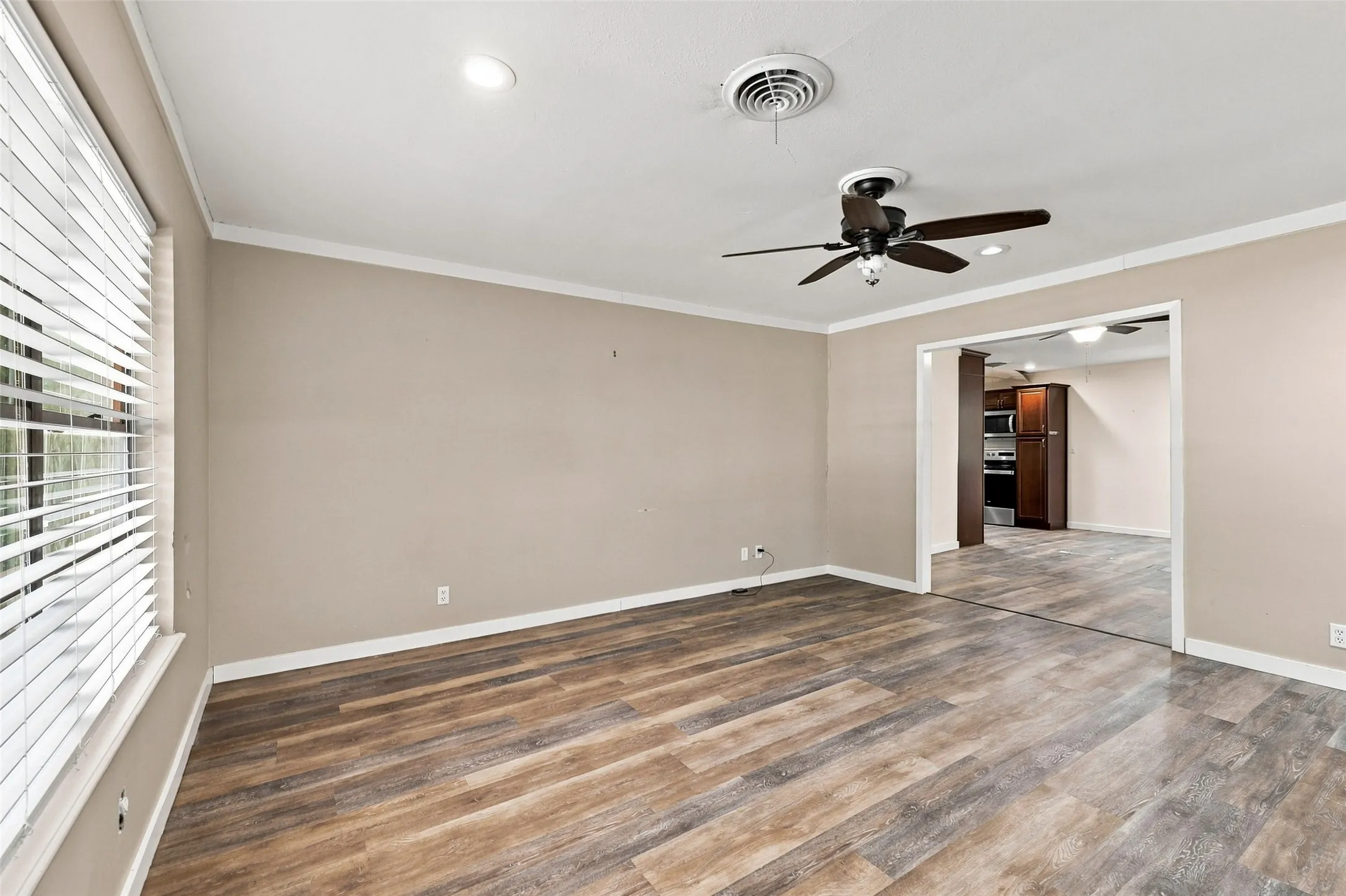 Wood-finish flooring, recessed lighting, ceiling fan, crown molding, and an open doorway