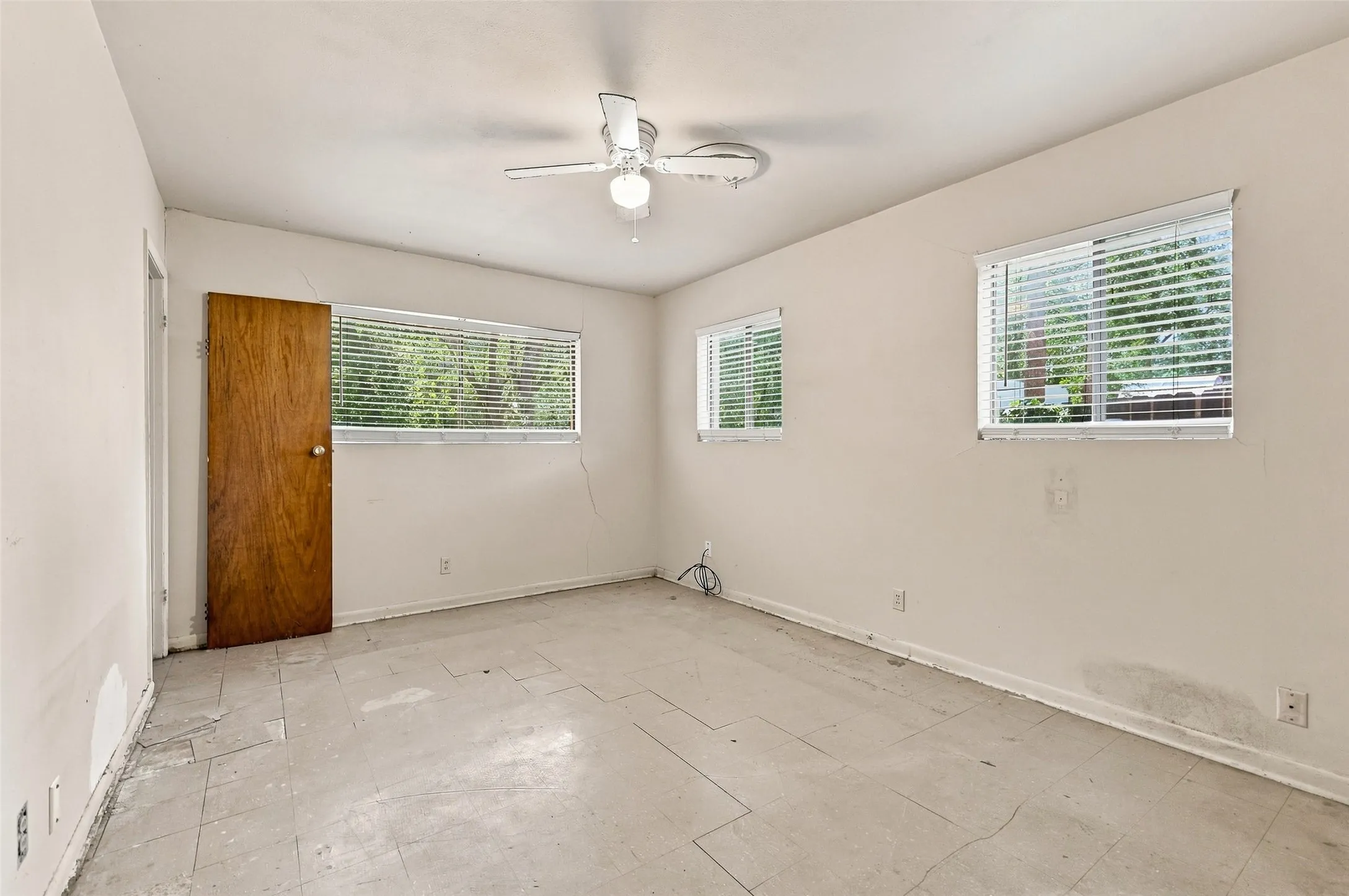 Room with multiple windows, ceiling fan, and a wood-finish door