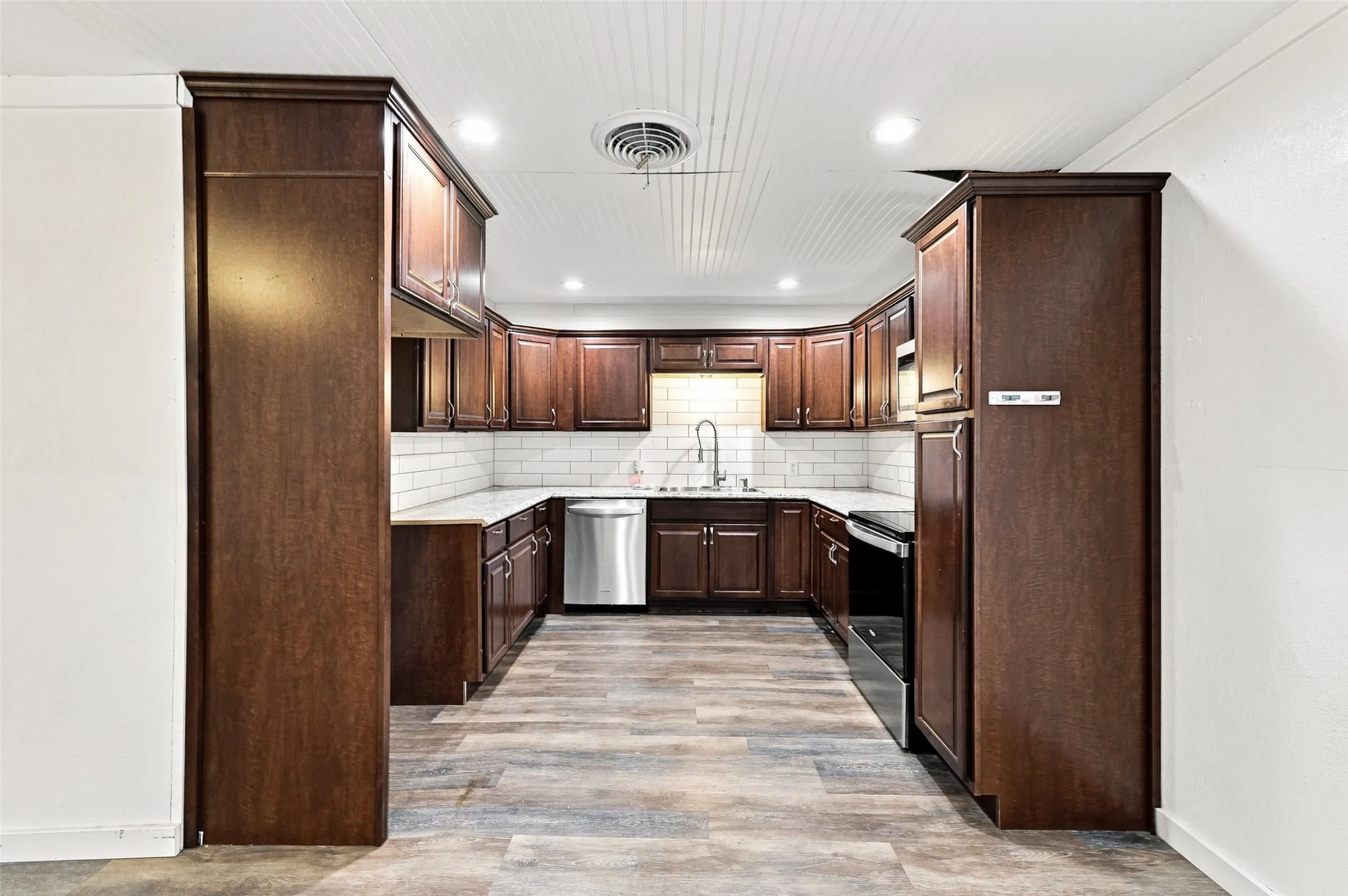 U-shaped kitchen with wood-finish flooring, dark wood cabinetry, and stainless steel appliances
