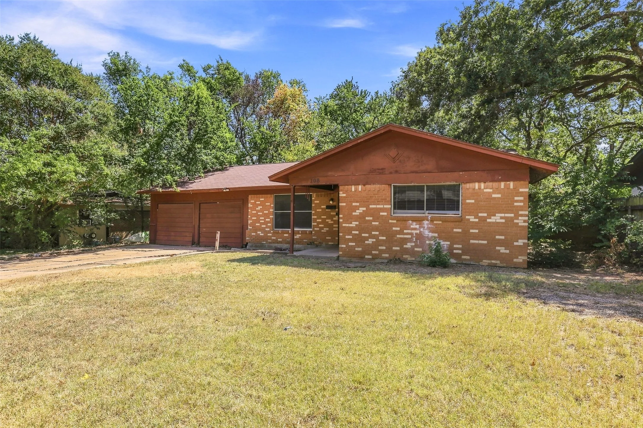 Brick facade with a contrasting white mortar pattern, pitched roofline, attached garage with two wooden doors, and a partial concrete driveway