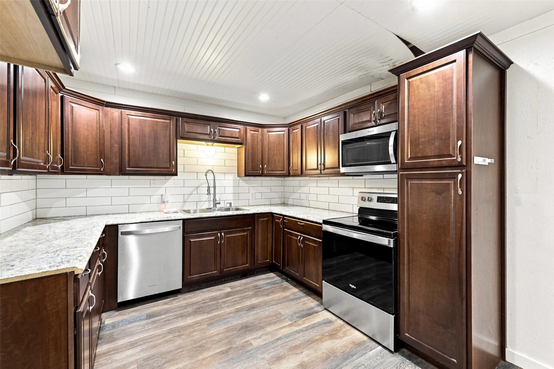 U-shaped kitchen with dark wood cabinetry, light granite countertops, white subway tile backsplash, and wood-finish flooring