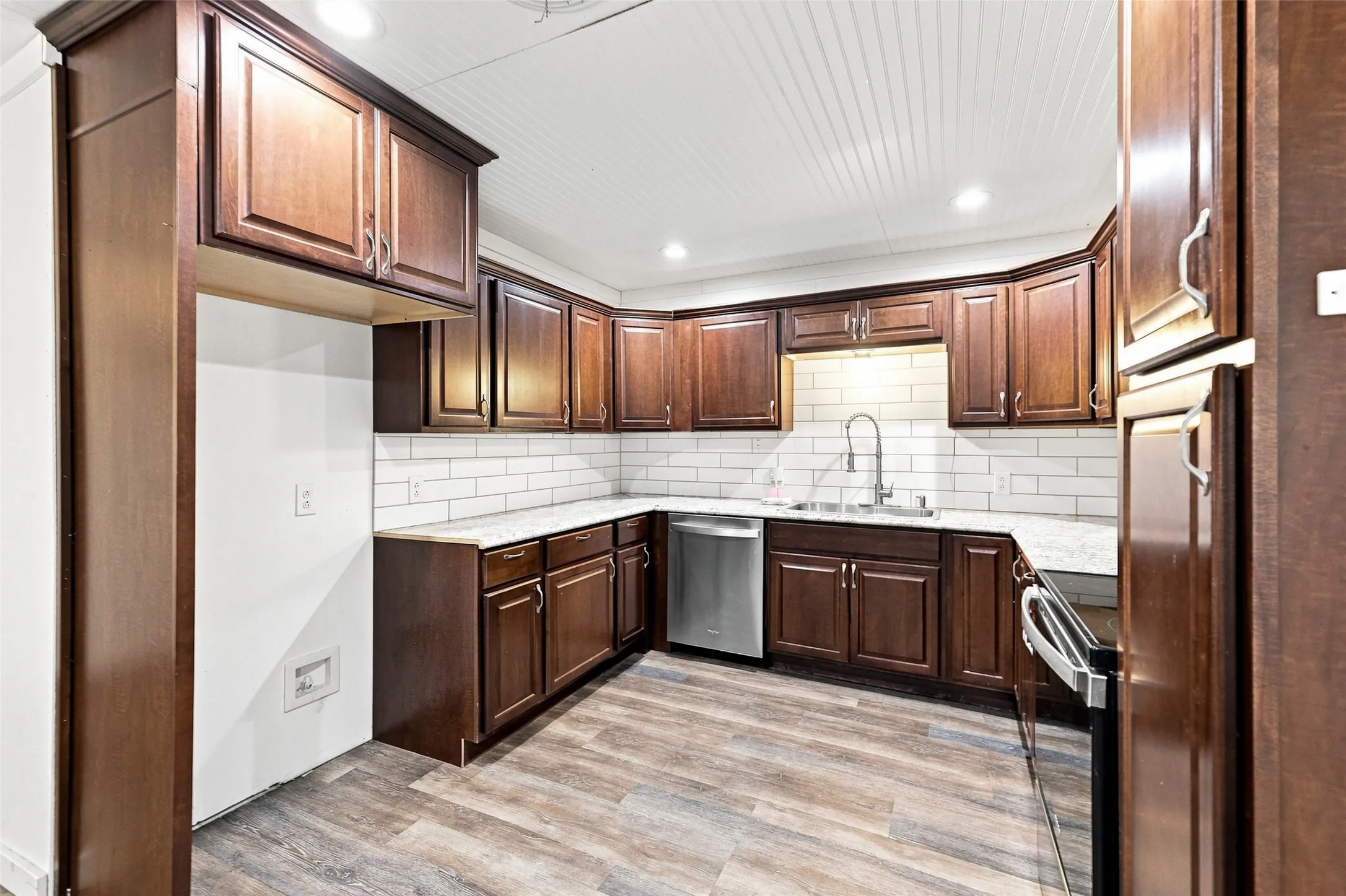 Kitchen featuring wood-finish flooring, wood cabinetry, subway tile backsplash, light-toned countertops, and recessed lighting