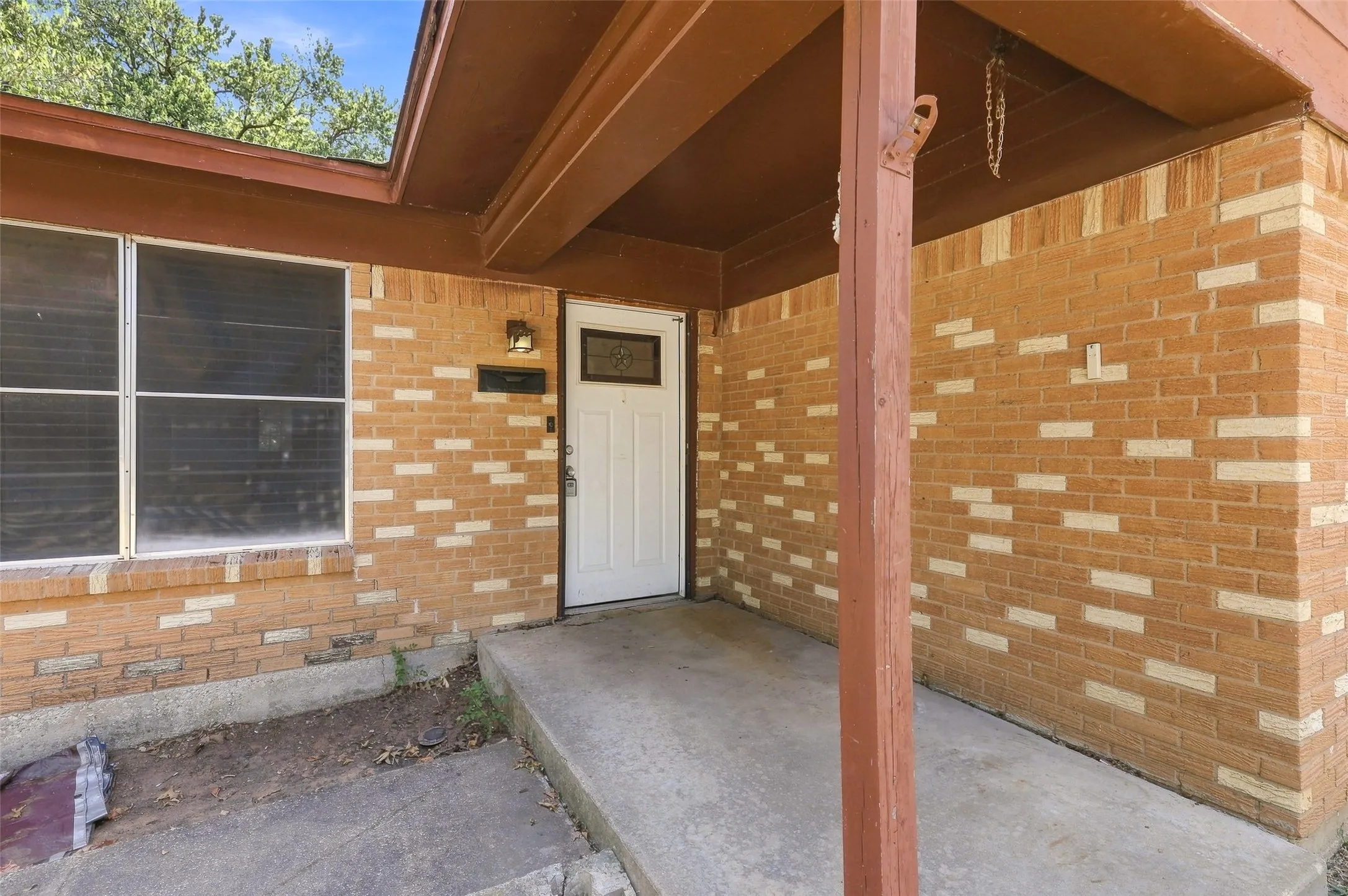 Brick exterior with decorative accents, covered entryway, white paneled front door with decorative glass, exterior wall sconce, and concrete porch