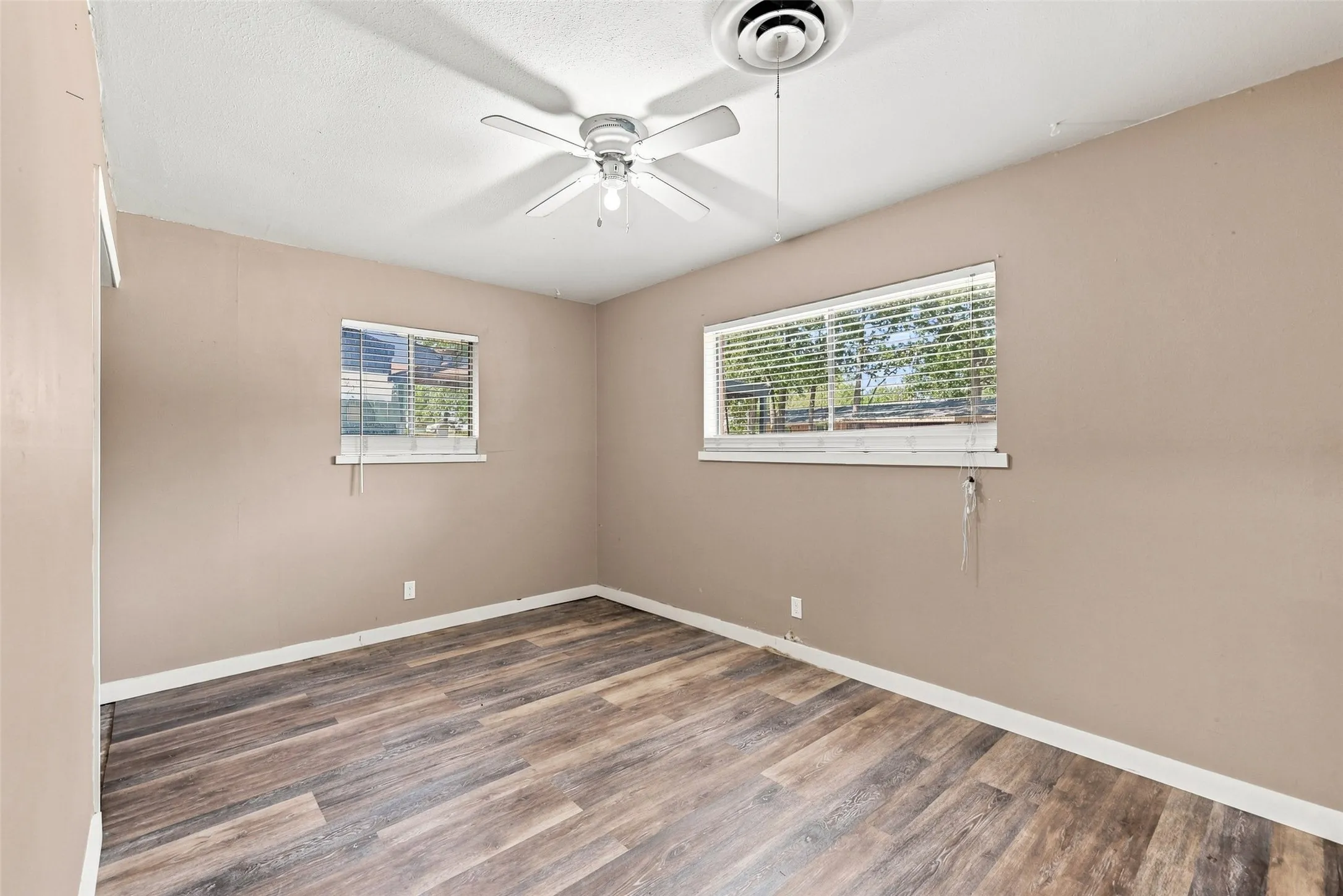 Wood-finish flooring, two windows with blinds, and a ceiling fan with integrated lighting