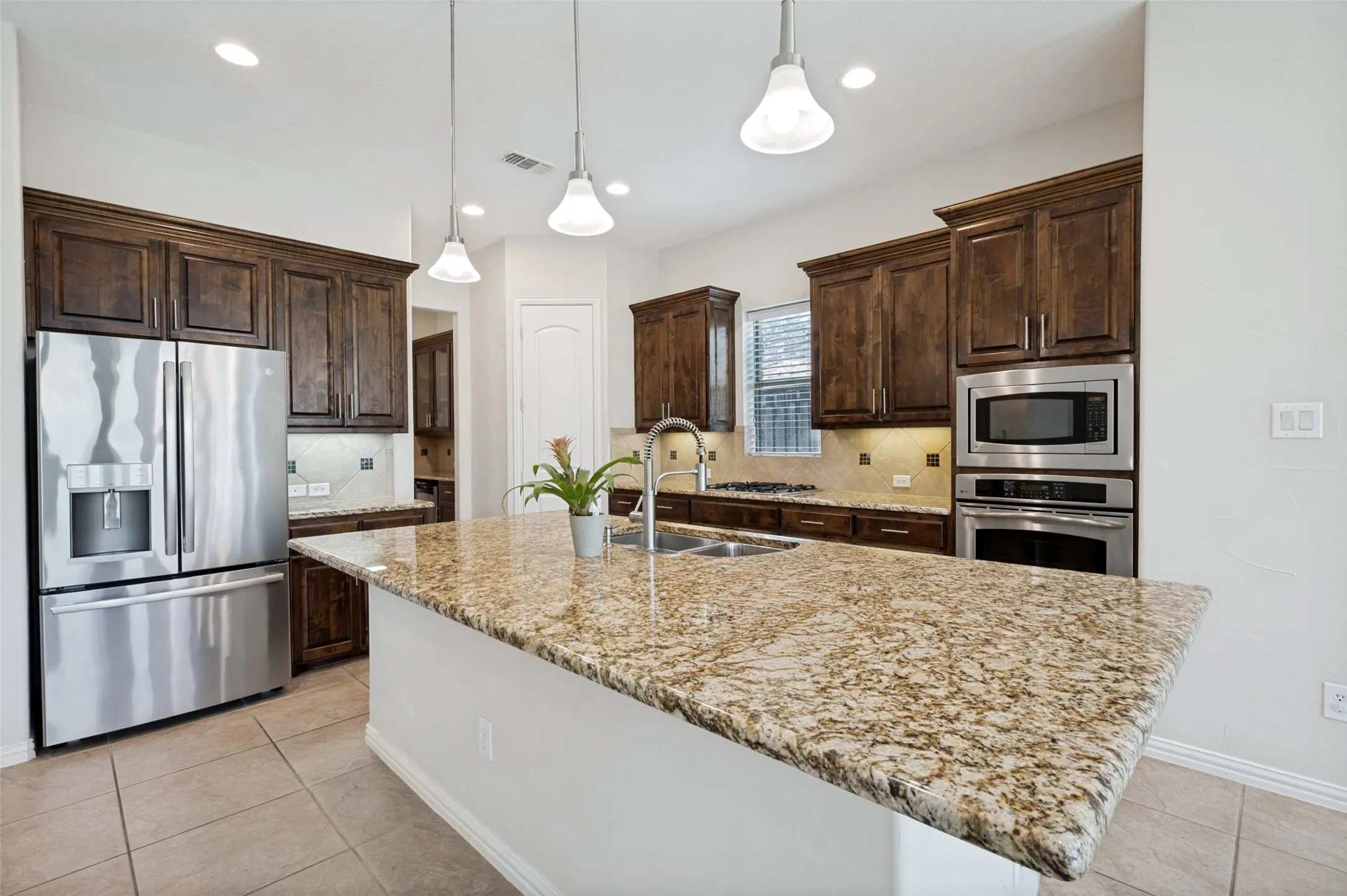 The chef's kitchen is designed to impress with a large granite island, rich custom cabinetry, stainless steel appliances, a gas cooktop, designer pendant lighting, and abundant counter space.