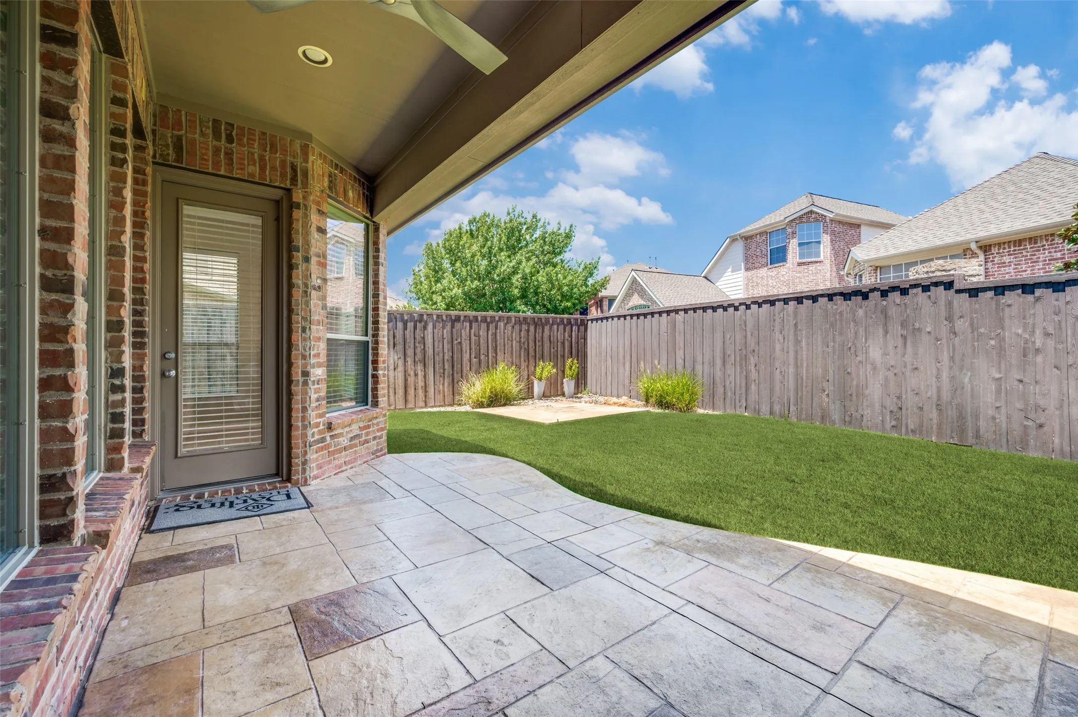 Covered back patio with stamped concrete, a ceiling fan for year-round comfort, and a spacious backyard with lush natural grass, offering the perfect setting for relaxing, entertaining, and outdoor enjoyment.