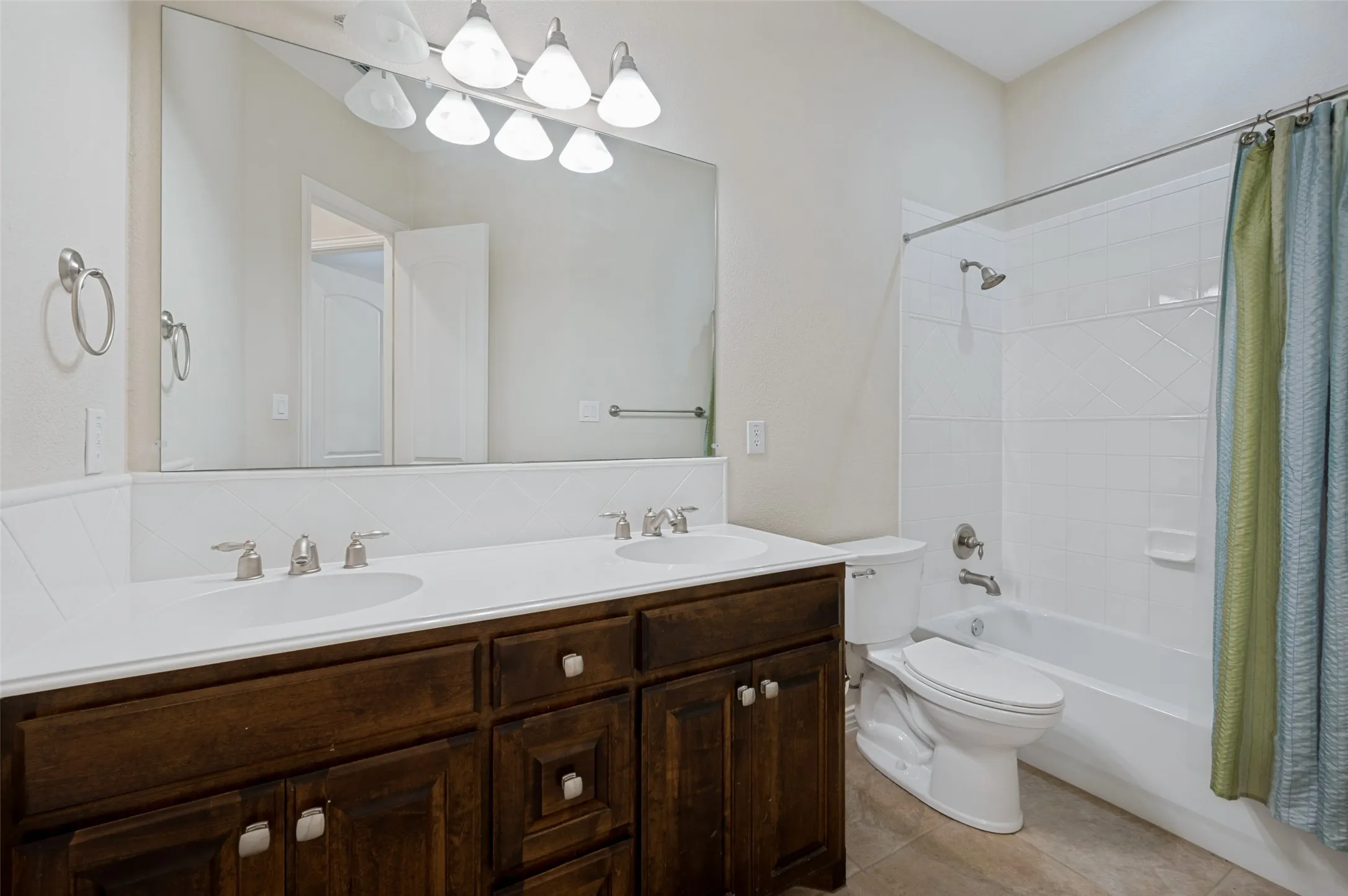 Spacious secondary bathroom featuring an oversized dual-sink vanity with abundant storage, a large mirror, and a shower/tub combination. Designed with both style and functionality in mind, this well-appointed bath provides plenty of space for family and guests while offering timeless finishes and everyday convenience.