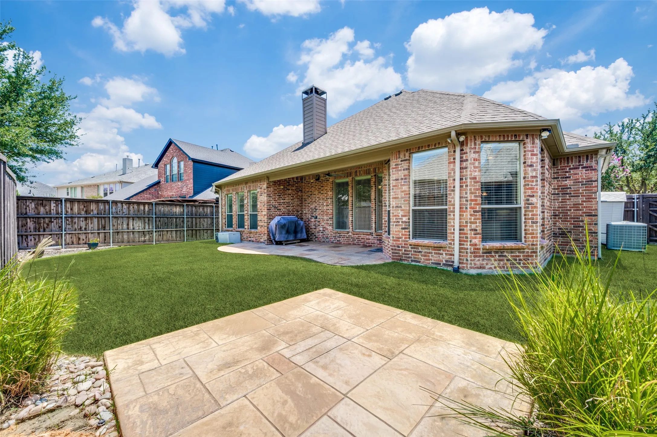 Spacious backyard with lush natural grass, a covered patio, and a stamped concrete platform that's perfect for a fire pit, outdoor seating, or entertaining family and friends.