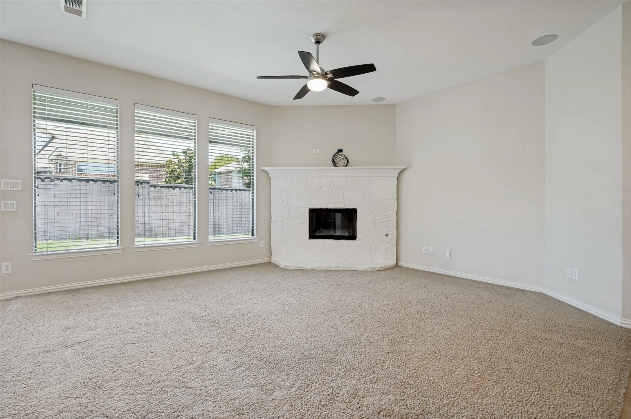 Spacious living room filled with natural light from a wall of oversized windows and centered around a stunning upgraded stone fireplace with raised hearth.