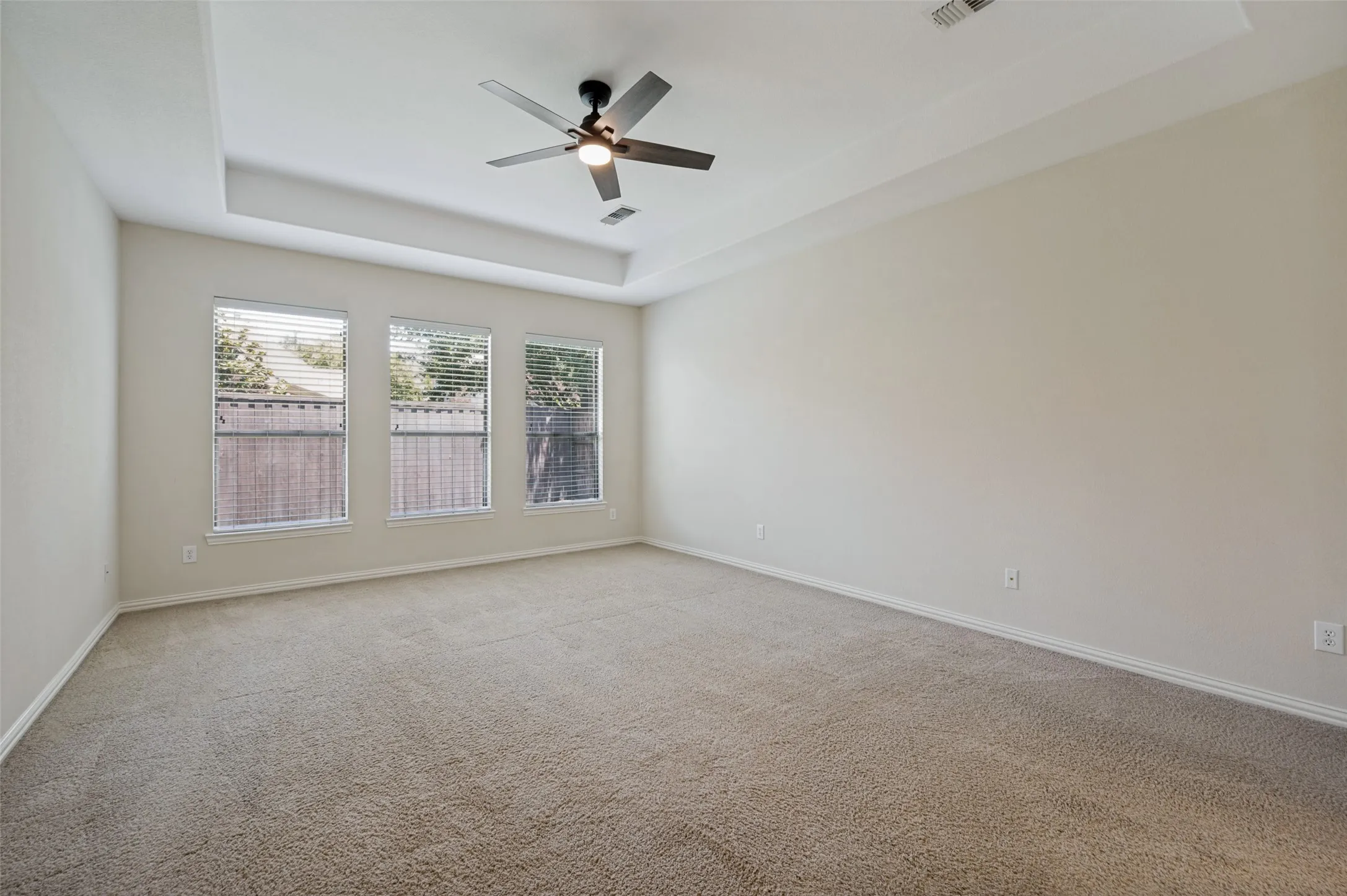Retreat to the spacious primary suite featuring an elegant tray ceiling, abundant natural light from a wall of windows, and plenty of room for a sitting area.
