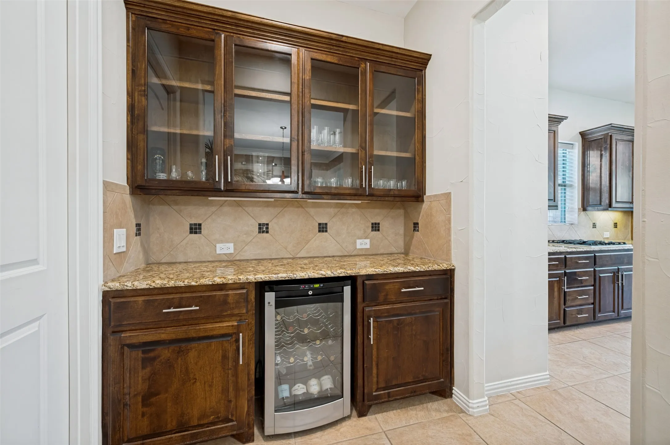 Entertaining is effortless with this dedicated serving area featuring custom cabinetry, granite countertops, glass-front upper cabinets, and a built-in beverage refrigerator.