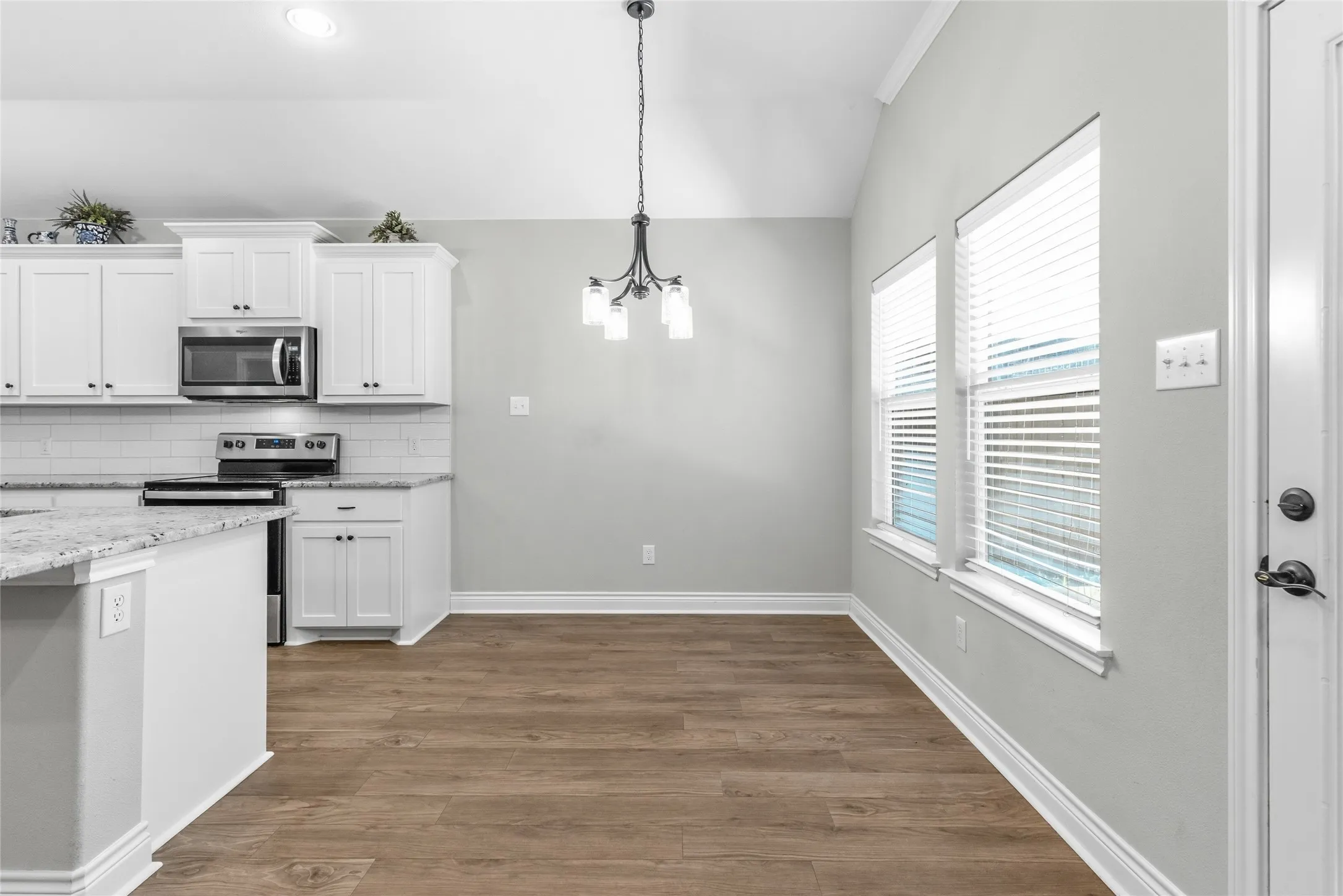 Open-concept kitchen and dining area featuring vaulted ceilings, wood-finish flooring, white cabinetry, and stainless steel appliances
