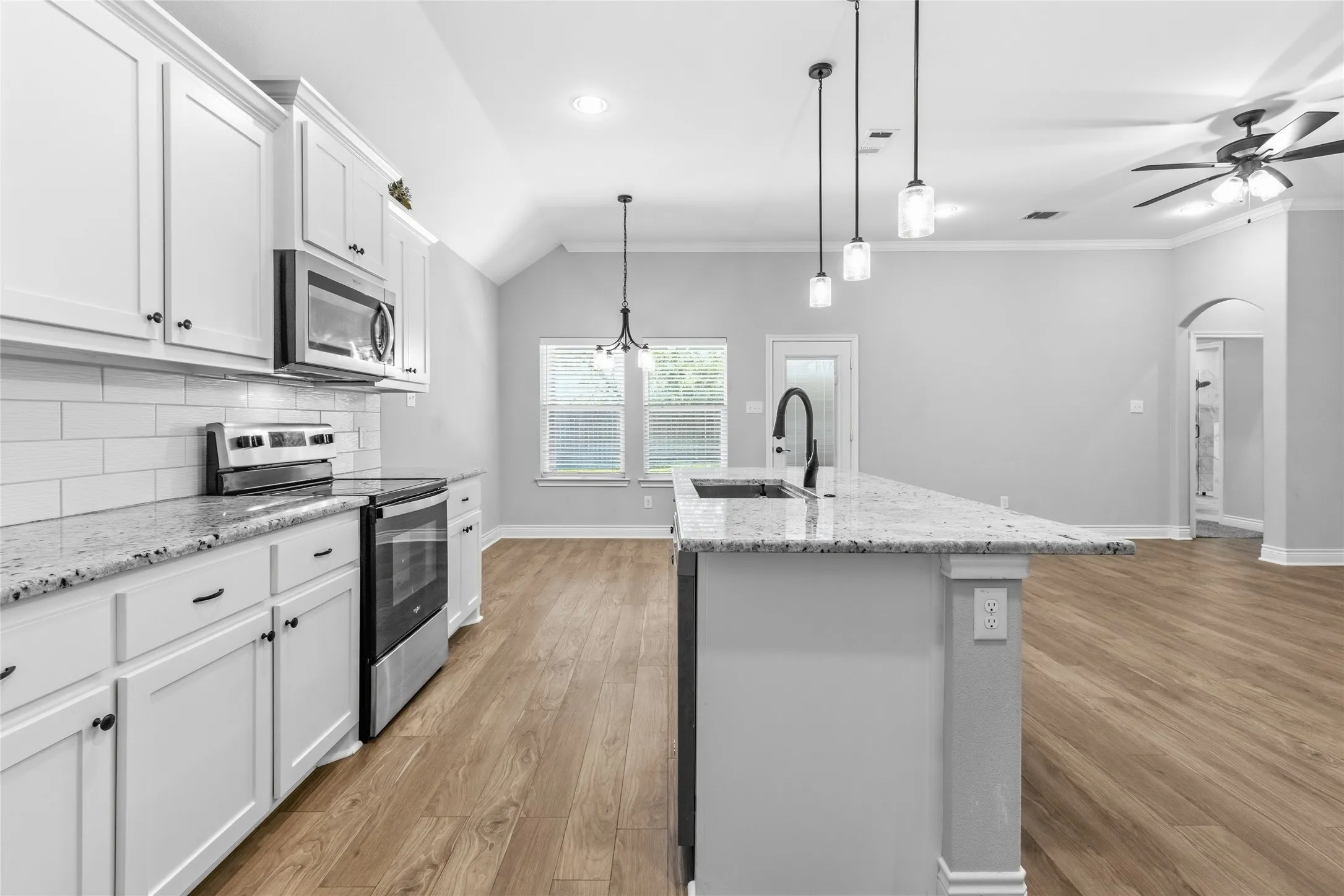 Kitchen featuring white shaker cabinetry, stainless steel appliances, granite countertops, subway tile backsplash, and wood-finish flooring