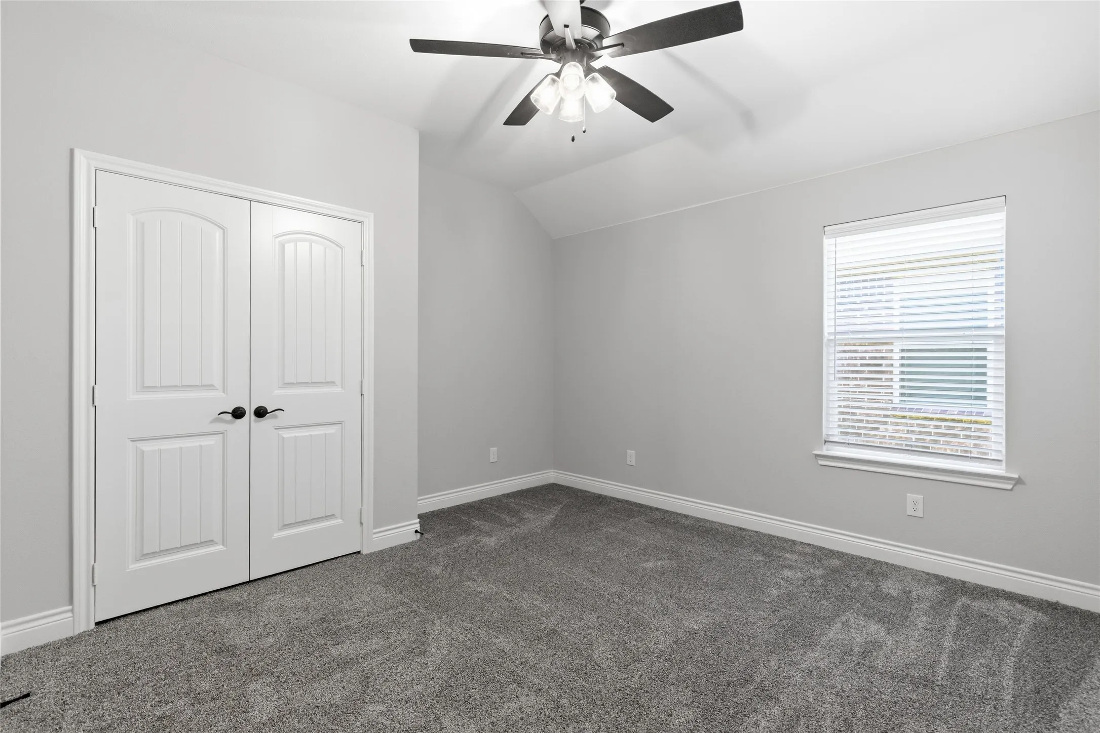 Spacious room featuring vaulted ceilings, a ceiling fan with integrated lighting, and a double-door closet with black hardware