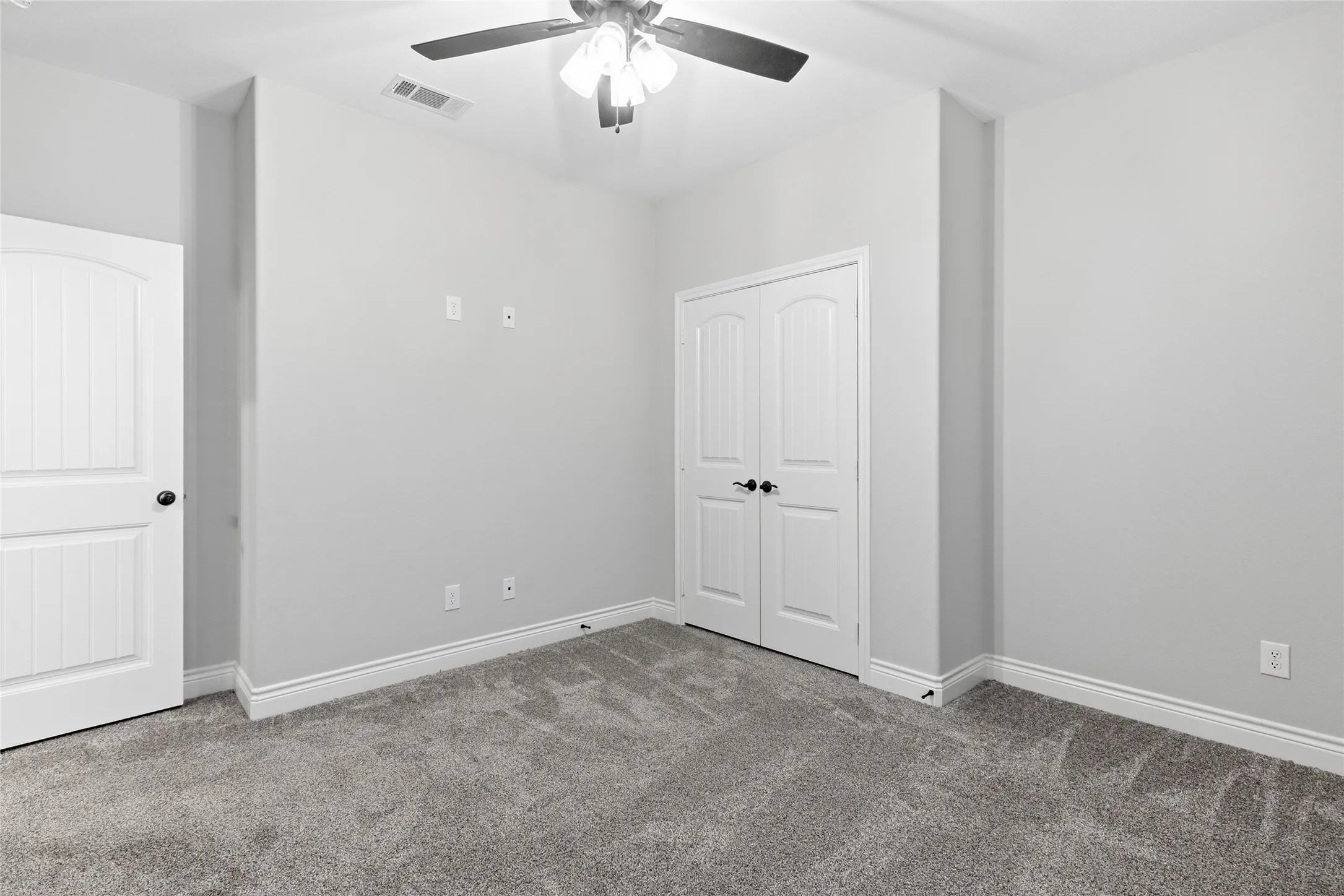 Room featuring light gray wall paint, gray patterned carpet, a ceiling fan with integrated lighting, white baseboards, and white paneled doors with black hardware