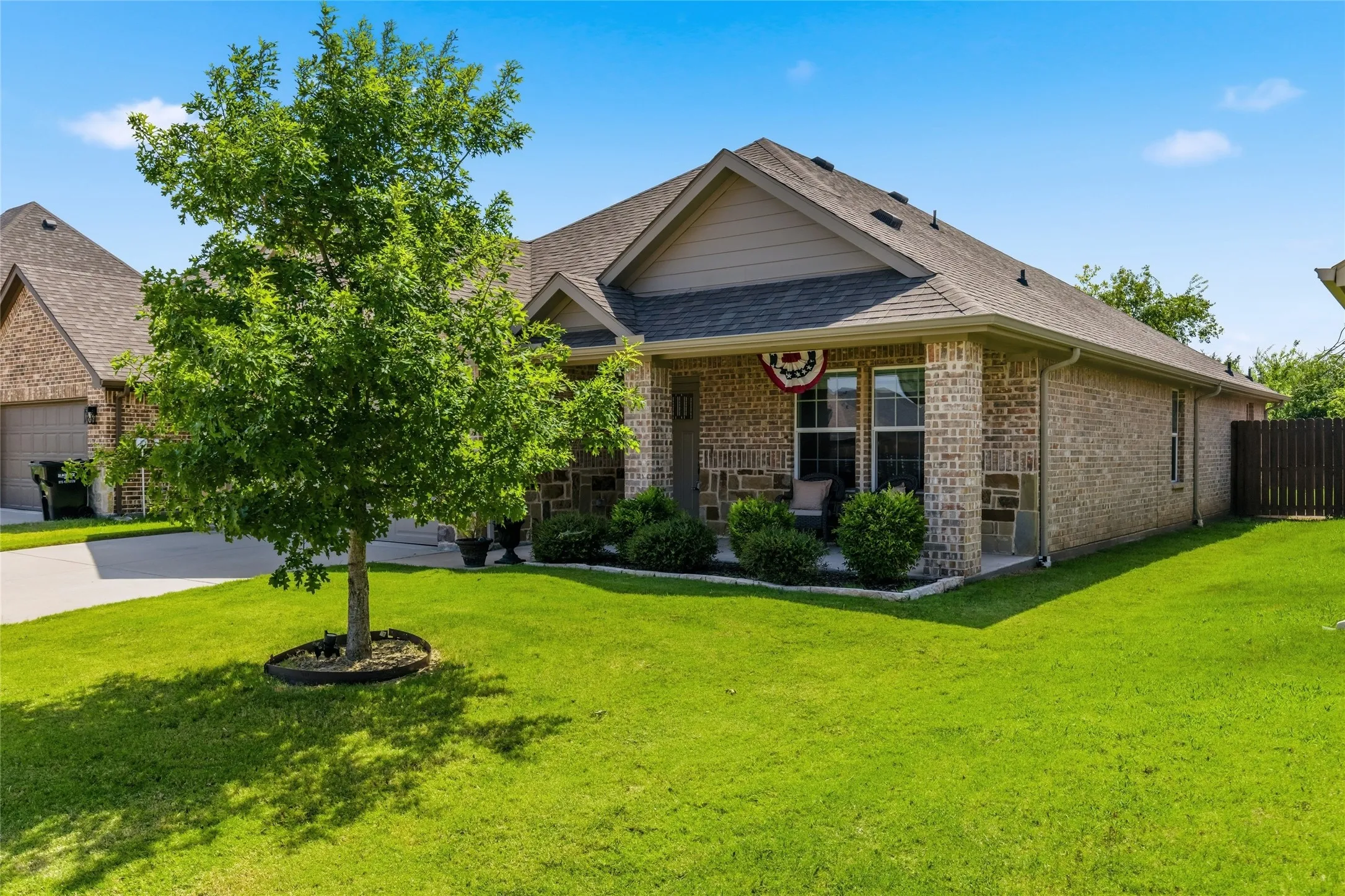 Brick and stone facade residence featuring a covered front porch, gabled roofline, and established landscaping