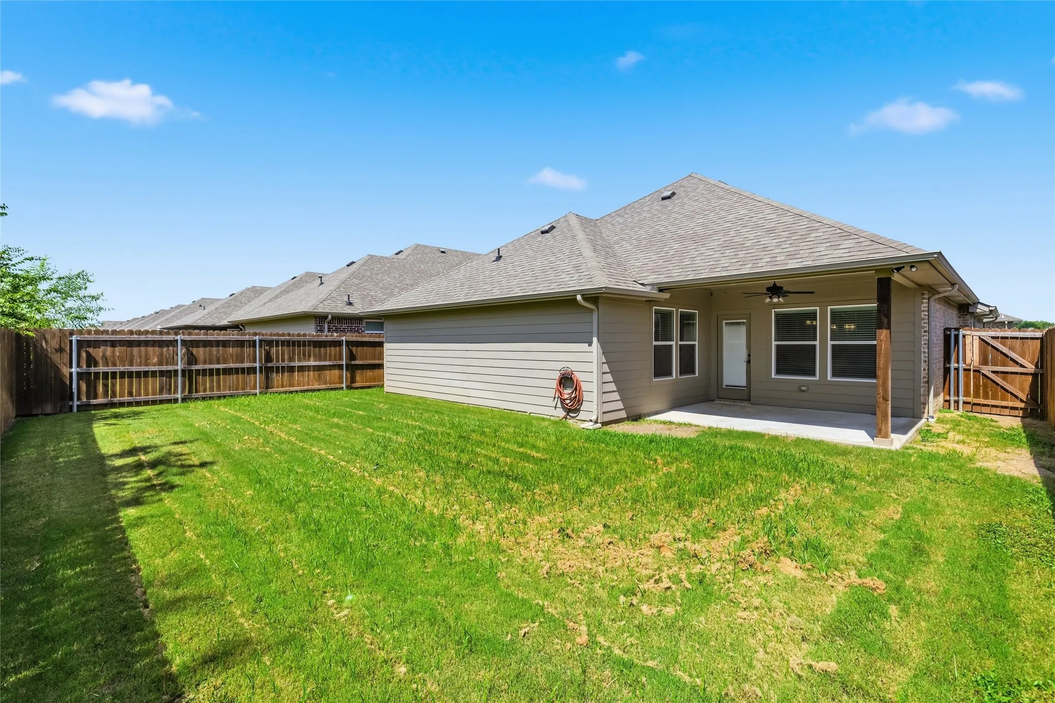 Expansive backyard with a manicured lawn, full wood fencing, and a covered patio featuring a ceiling fan