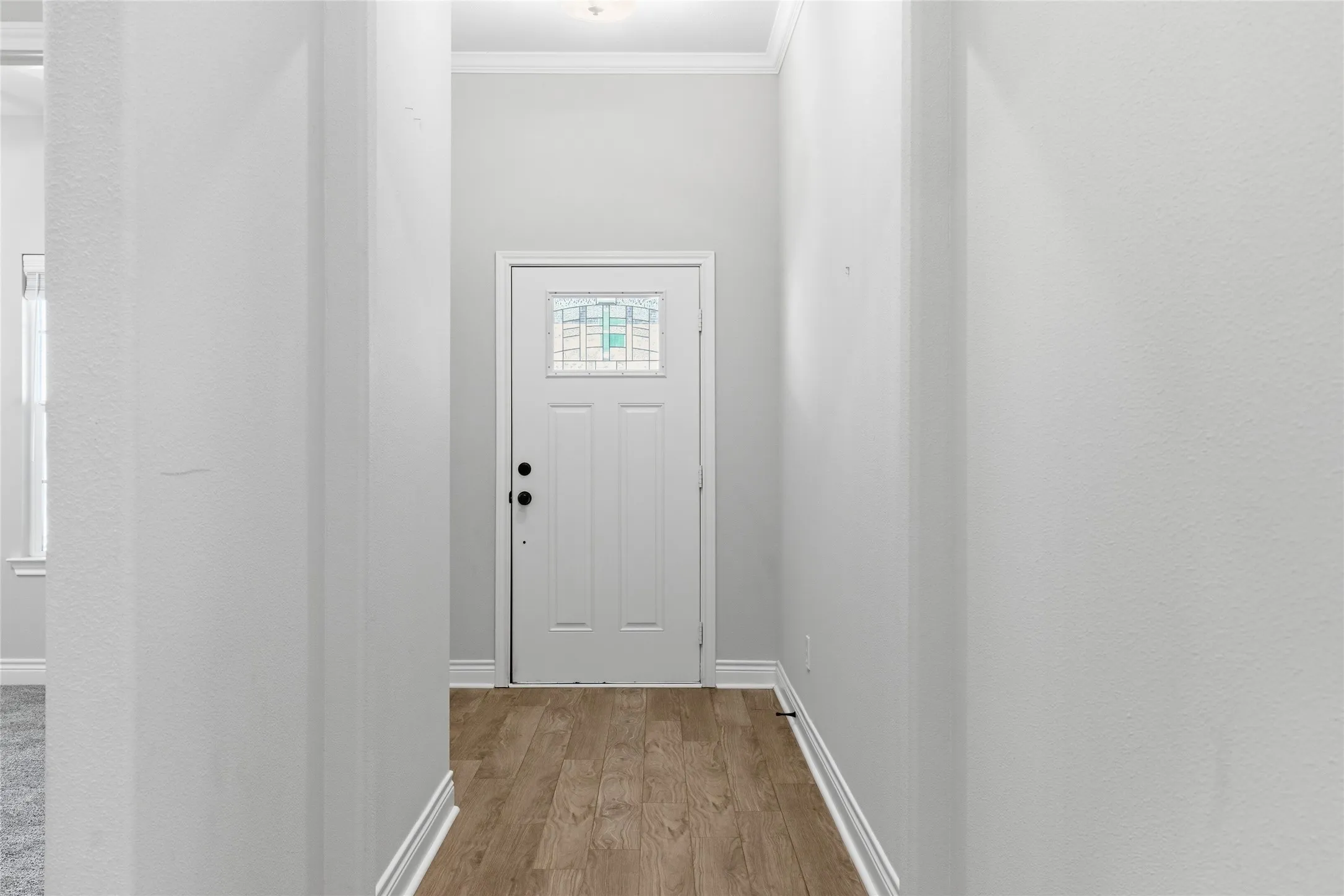 Inviting entry hall featuring wood-finish flooring, crisp white trim, and a front door with a decorative glass insert