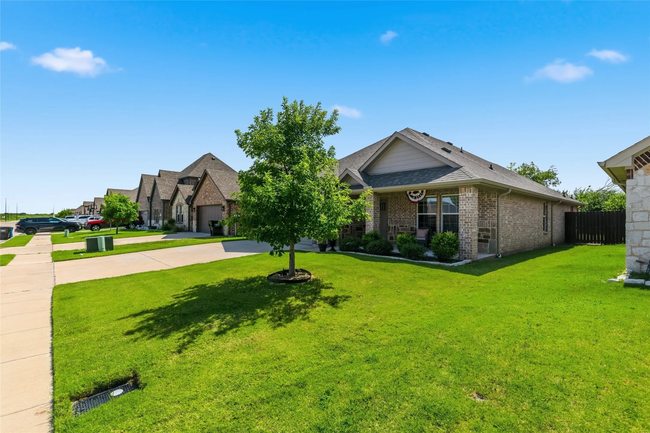 Brick exterior home featuring a covered front porch, mature landscaping, sidewalk, and a spacious front lawn