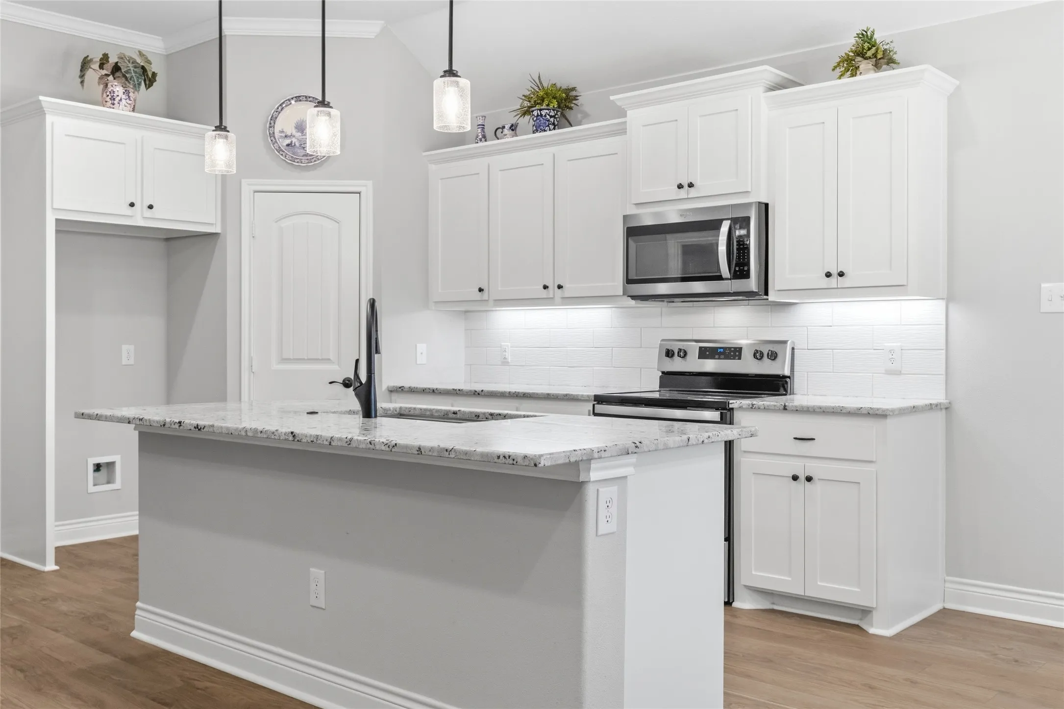 Kitchen featuring an expansive island with a waterfall countertop, white shaker cabinetry, stainless steel appliances, and wood-finish flooring