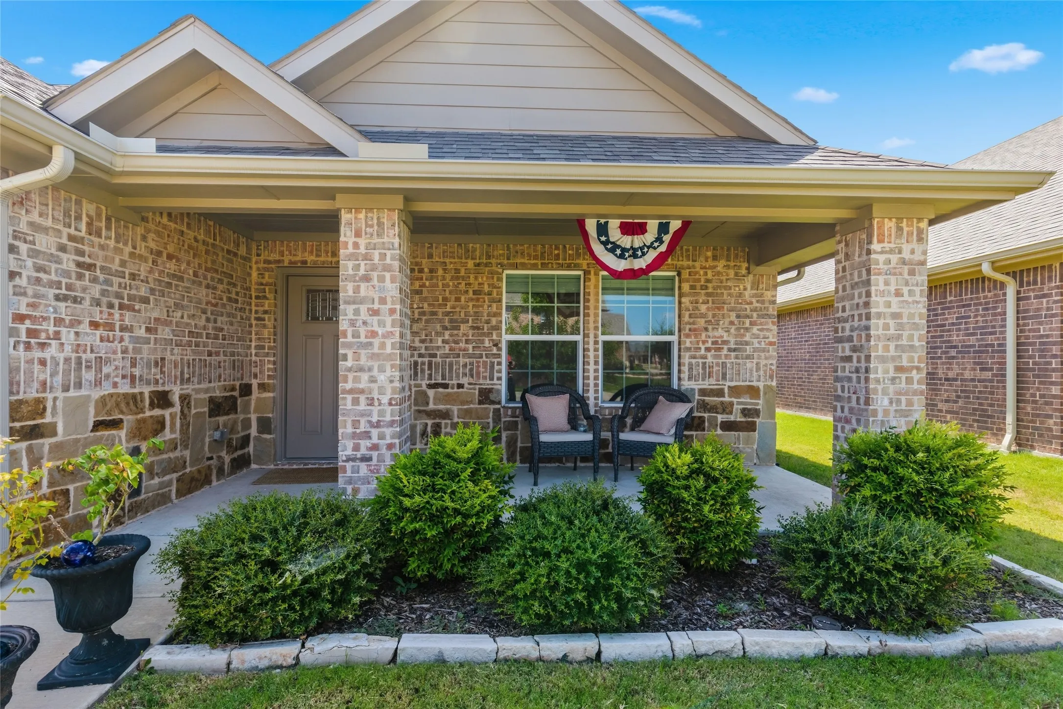 Brick and stone facade with a covered porch entry, architectural roofline, and front landscaping