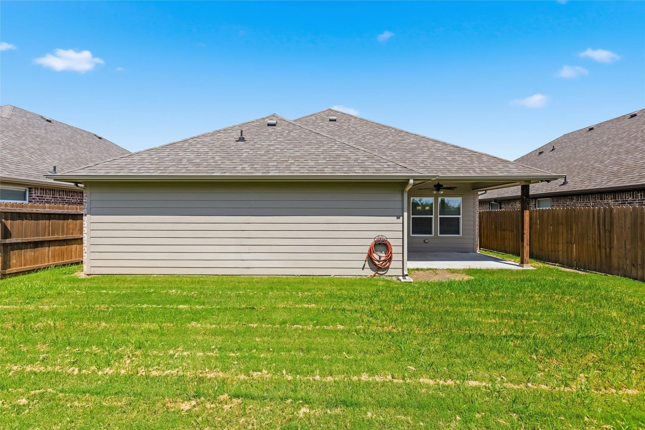 Expansive green lawn surrounds the rear of the property, featuring a covered patio with a ceiling fan