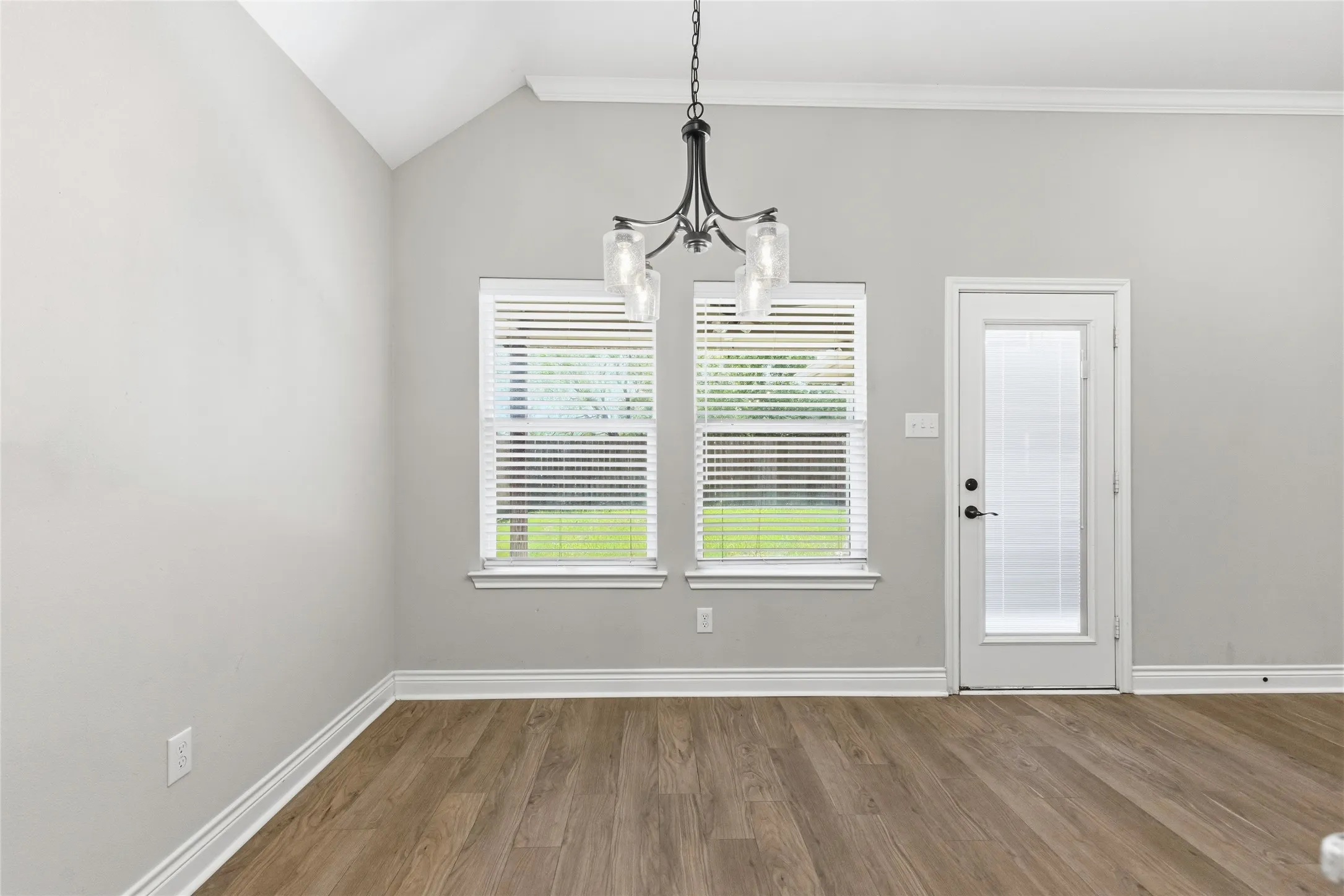 Room featuring vaulted ceilings, wood-finish flooring, and a glass-paneled door