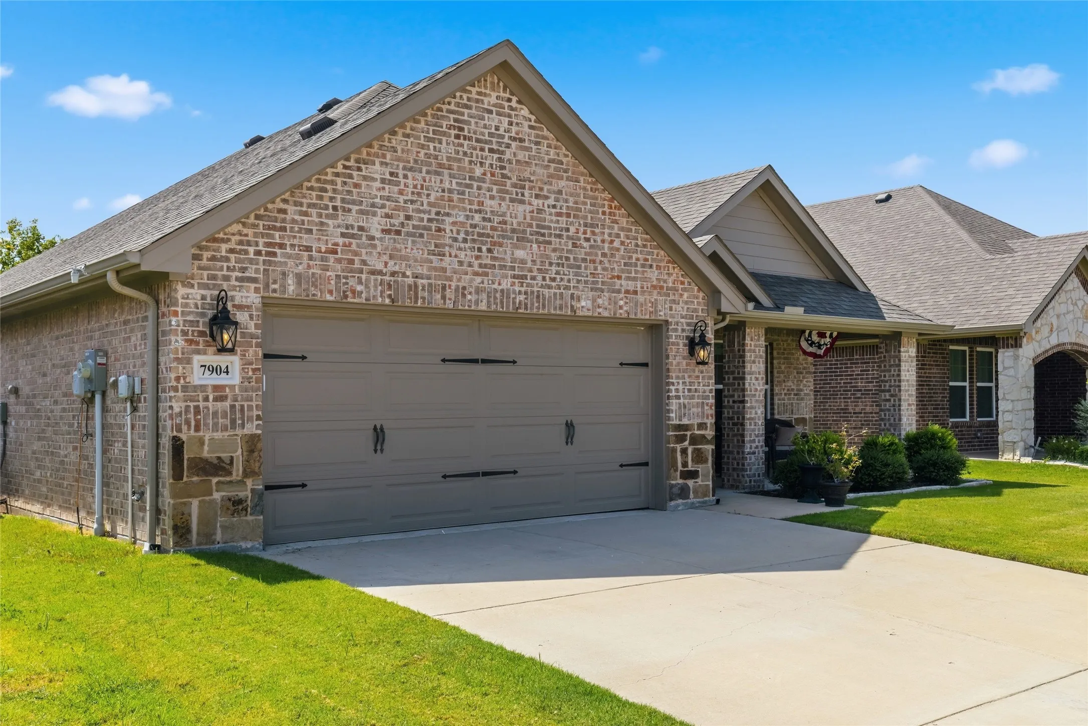 Brick and stone facade featuring an attached garage with carriage-style door, concrete driveway, and covered front entry