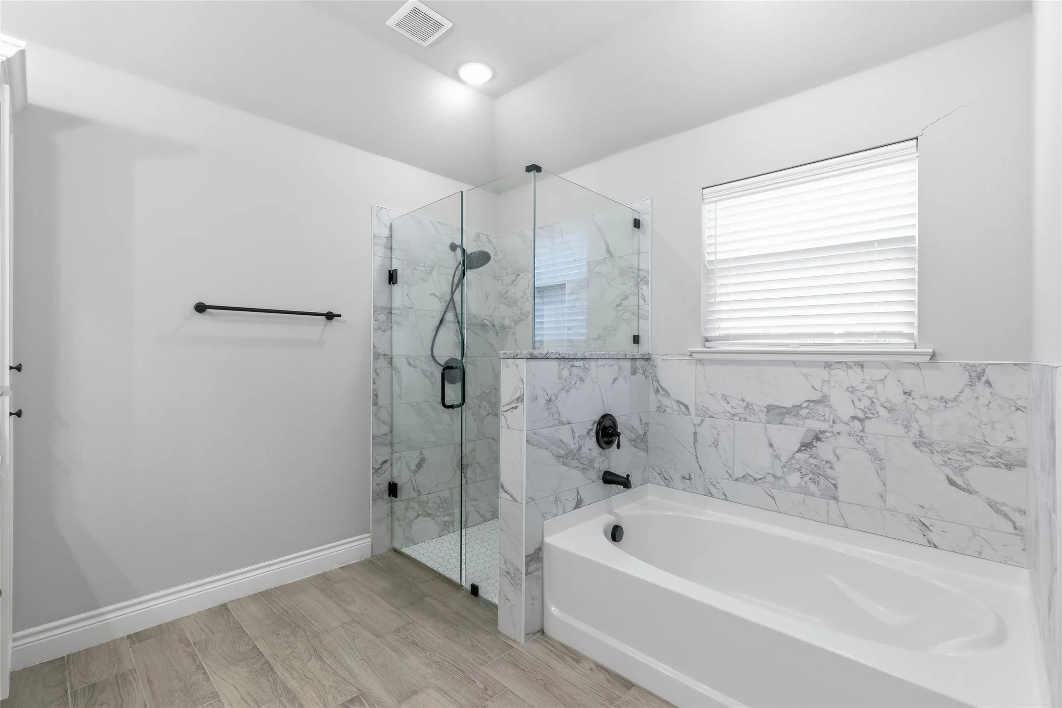 Full bathroom featuring a walk-in shower with clear glass enclosure, a built-in bathtub, and marble-look wall tiling