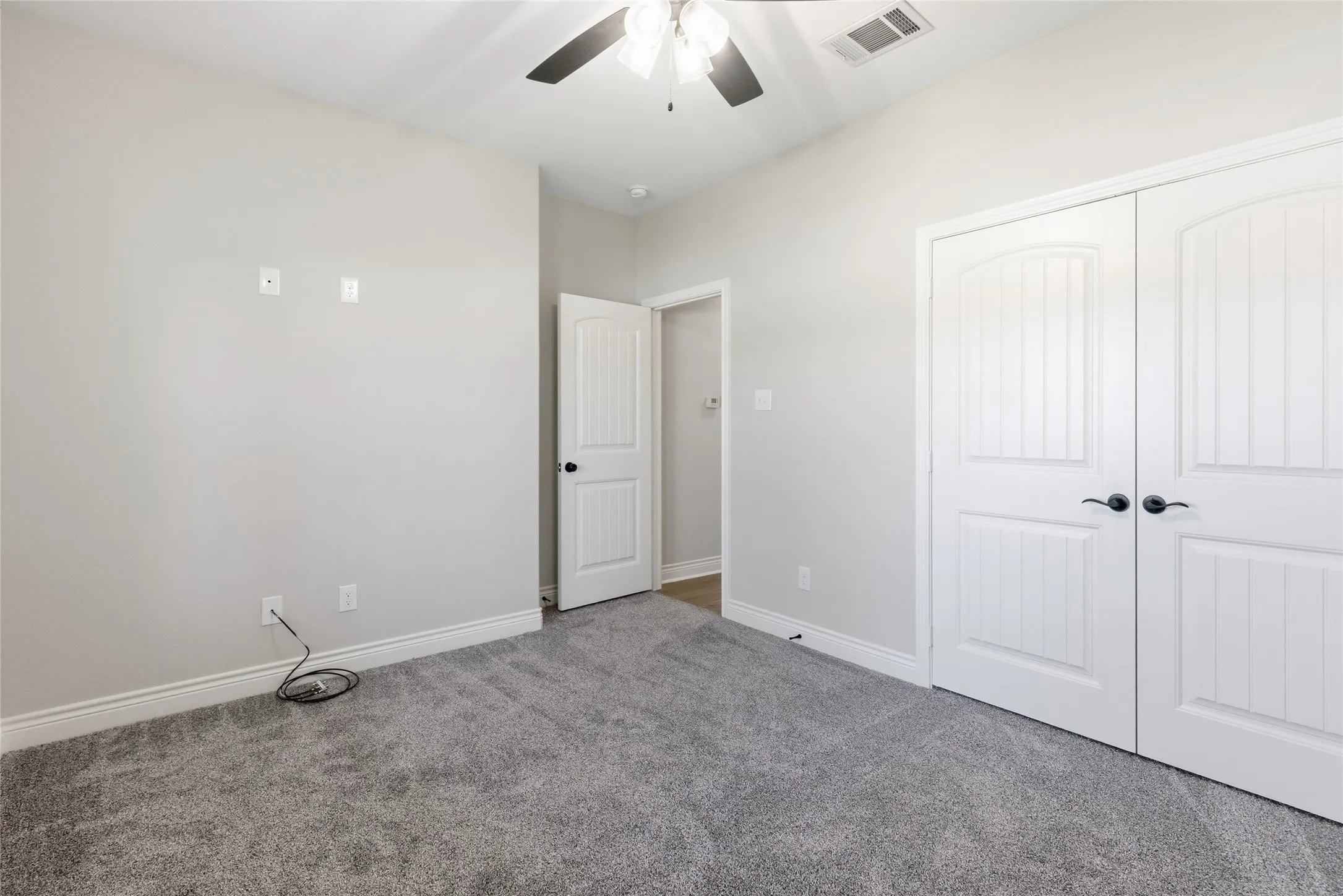 Carpeted room featuring white paneled double doors, a white paneled interior door, and a ceiling fan with integrated lighting