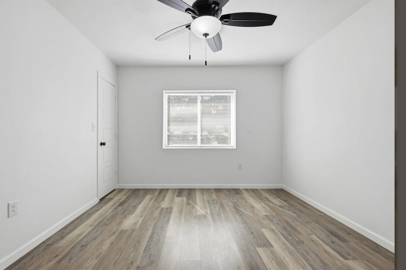 Bright room featuring wood-finish flooring, a contemporary ceiling fan with integrated lighting, a multi-pane window, and a white paneled door with black hardware