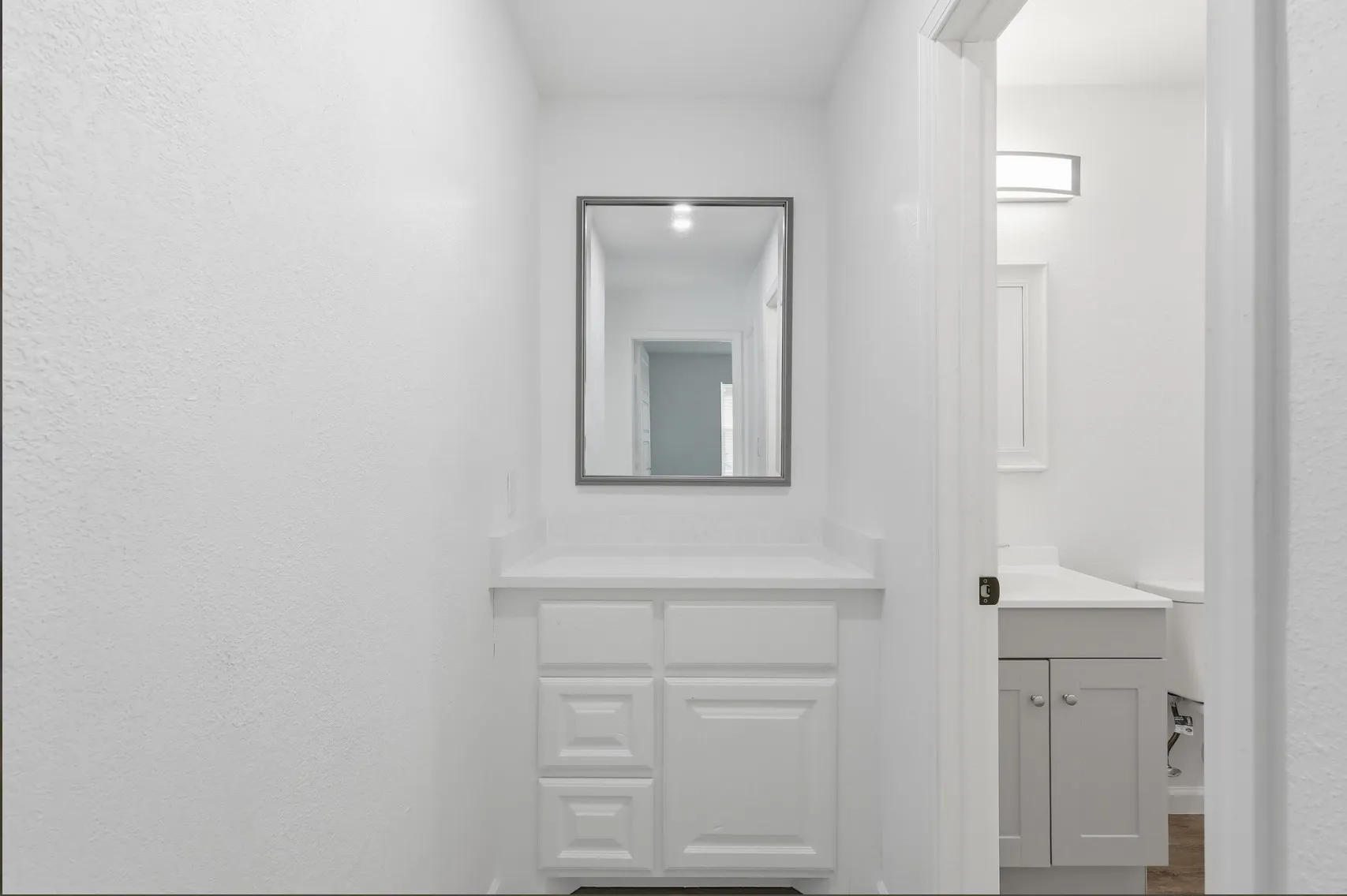 Vanity area featuring a white cabinet with paneling, a light-toned countertop, and a framed mirror