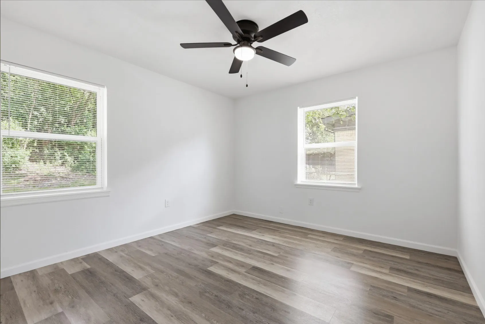 Room featuring wood-finish flooring, white walls, and a ceiling fan with integrated lighting
