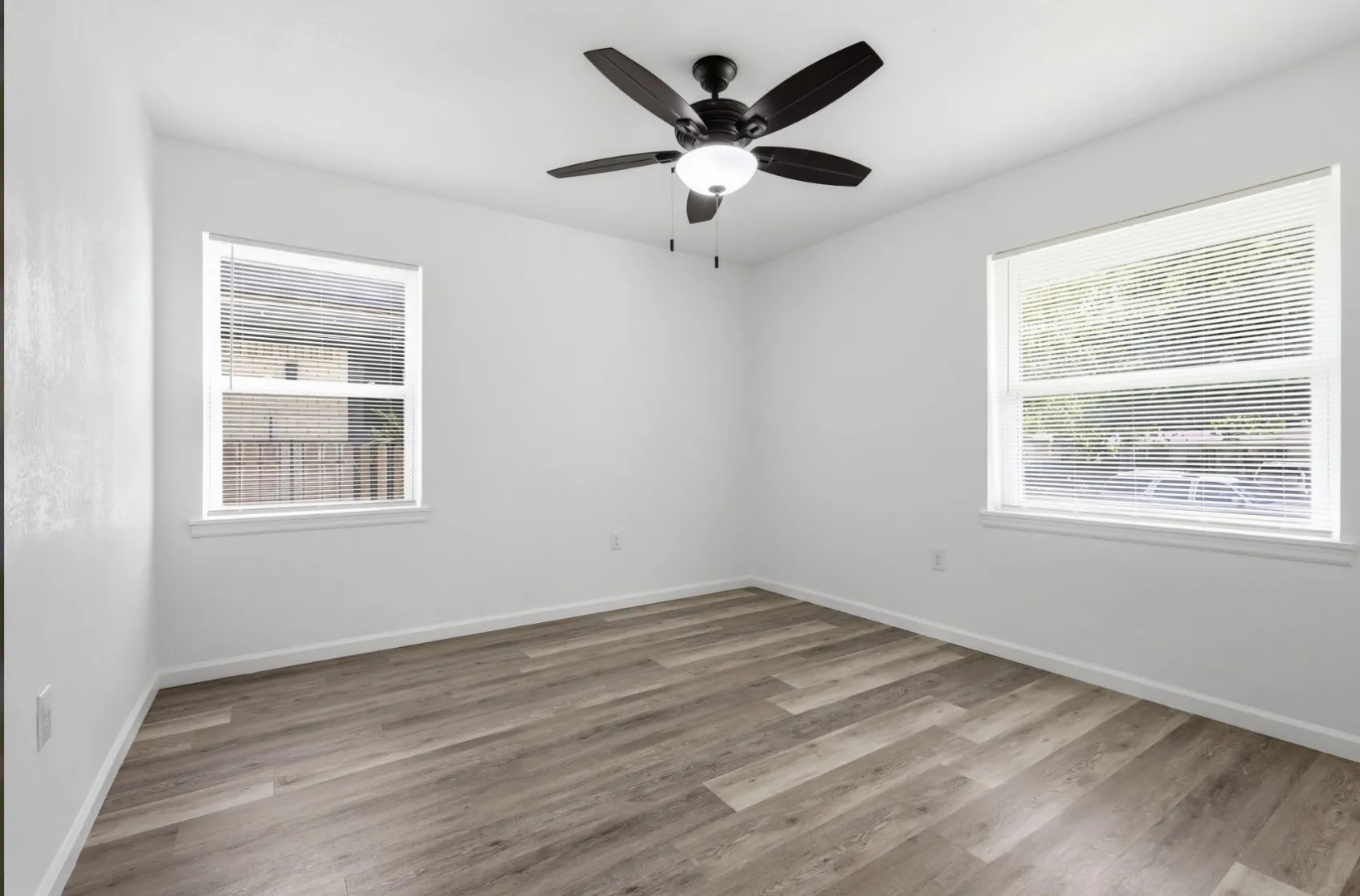 Room featuring wood-finish flooring, white walls, and a dark-toned ceiling fan with integrated lighting