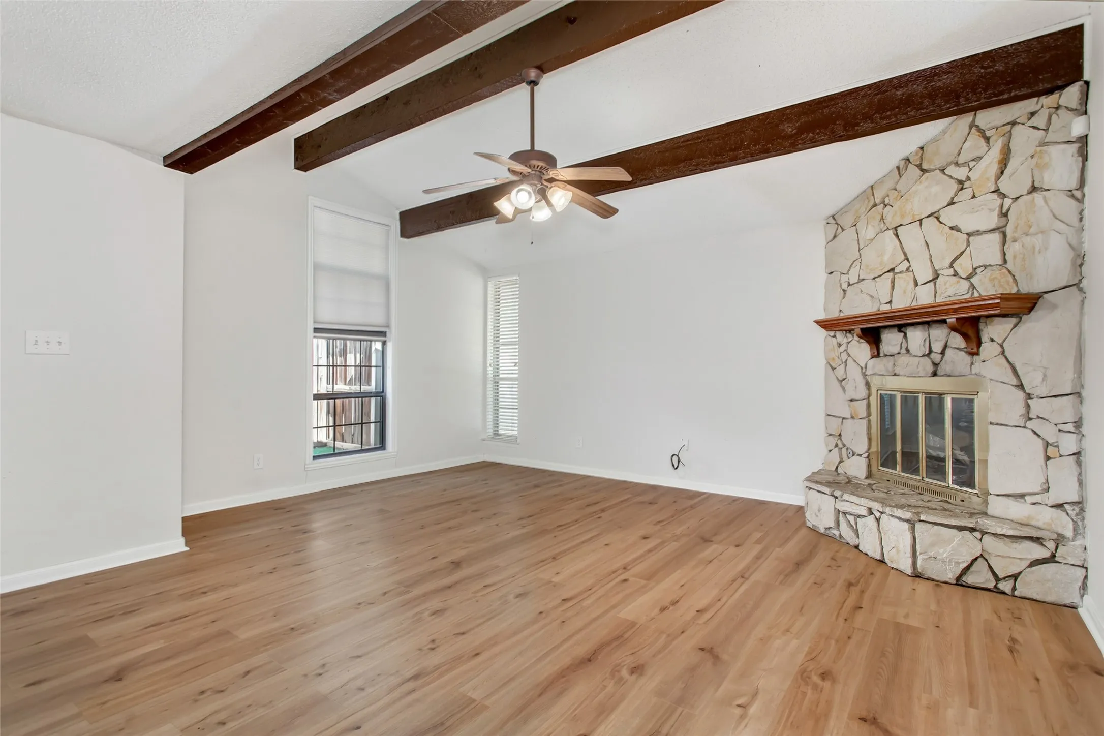 Spacious living room with vaulted ceiling, exposed wood beams, wood-burning stone fireplace, and updated wood like laminate flooring.