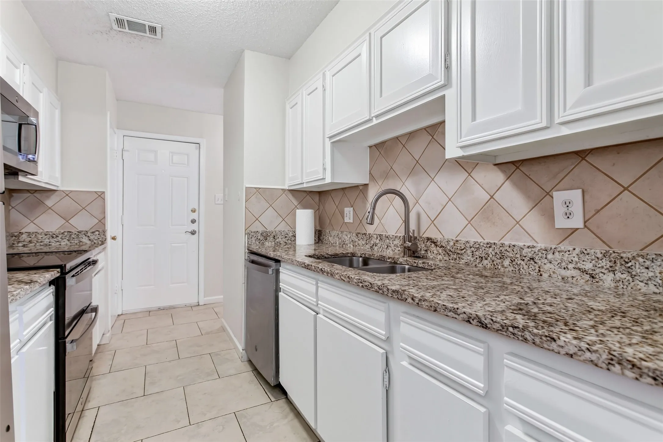 Galley kitchen featuring granite countertops, white cabinetry, stainless appliances, and tile backsplash.