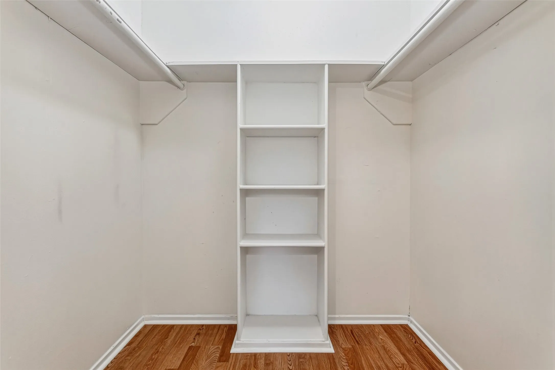 Large walk-in closet with built-in shelving and dual hanging rods for organized storage.
