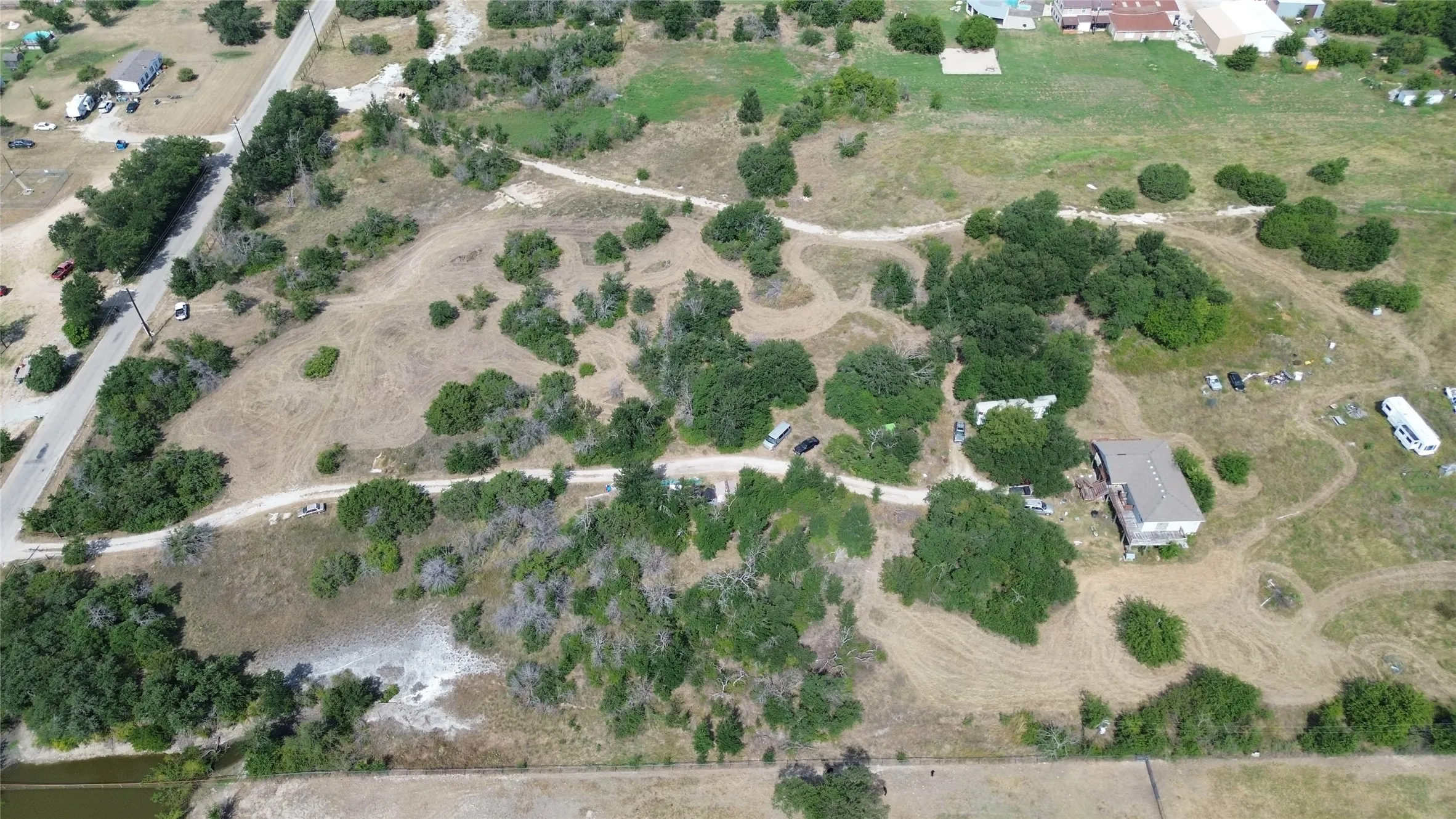 Expansive property featuring a single-family residence with a light-colored roof, multiple mature trees, and unpaved access paths