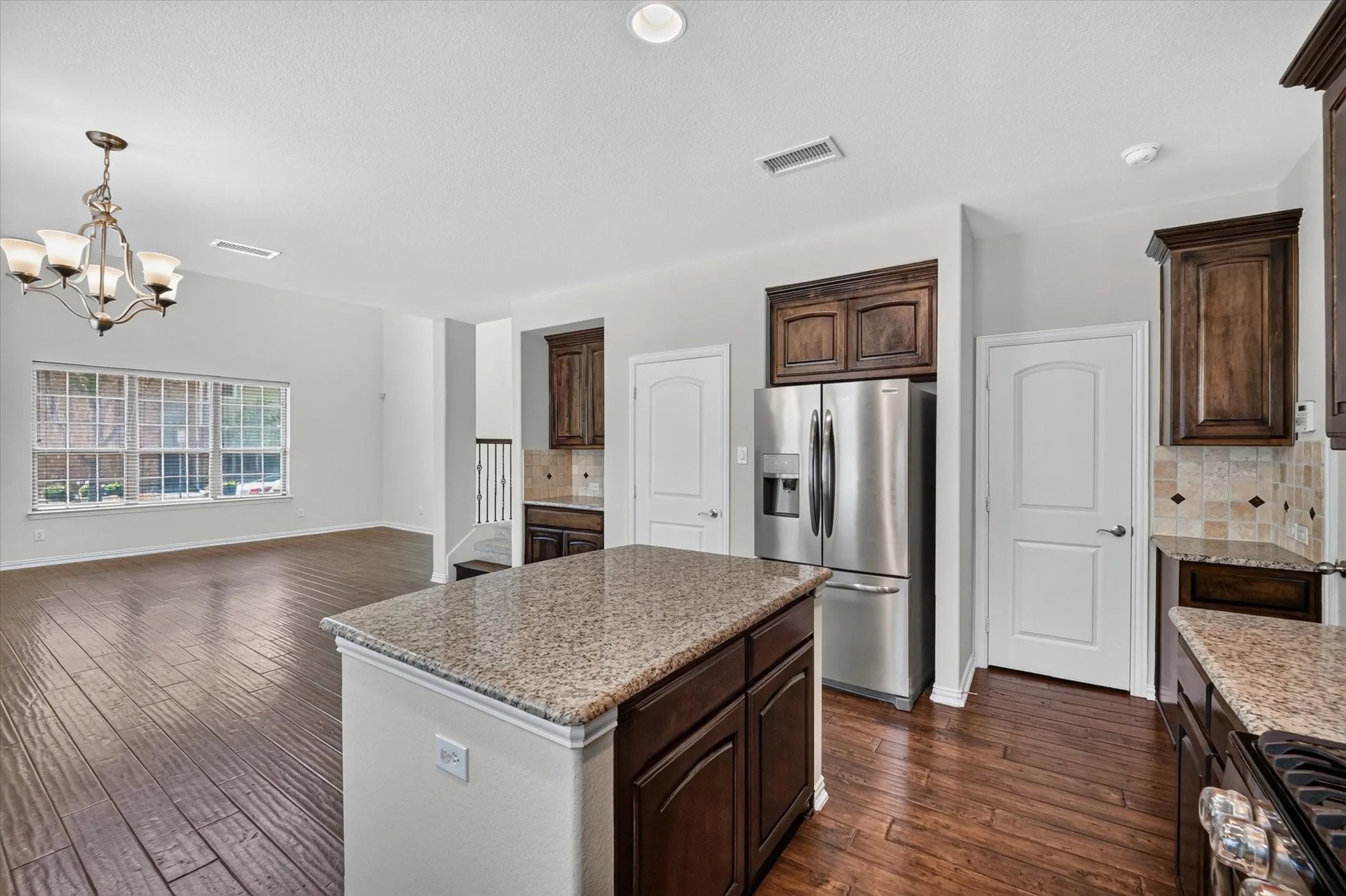 Kitchen island with granite countertop, rich wood-finish cabinetry, and stainless steel refrigerator